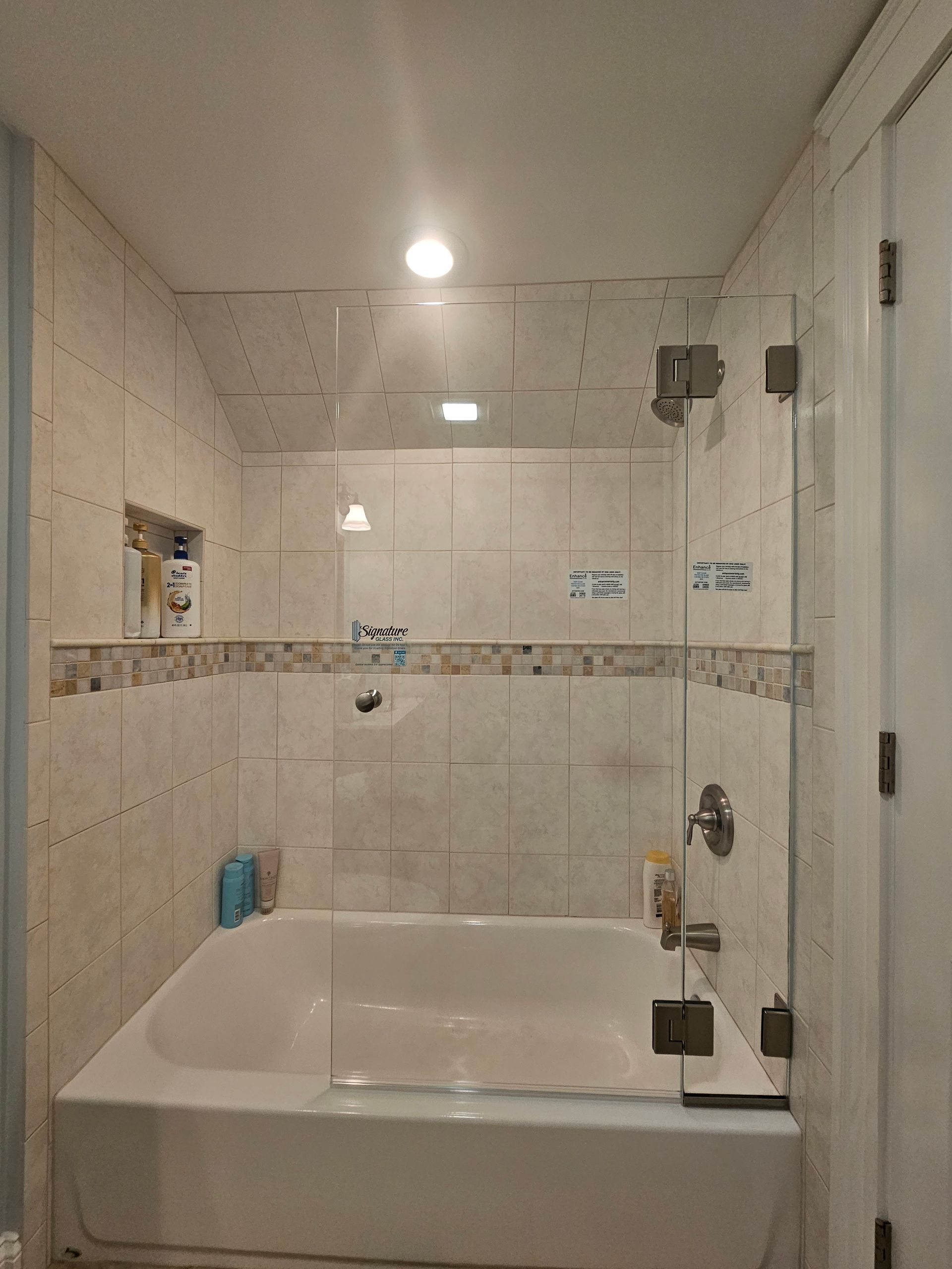 Bathroom with a white bathtub, glass shower doors, and tiled walls.