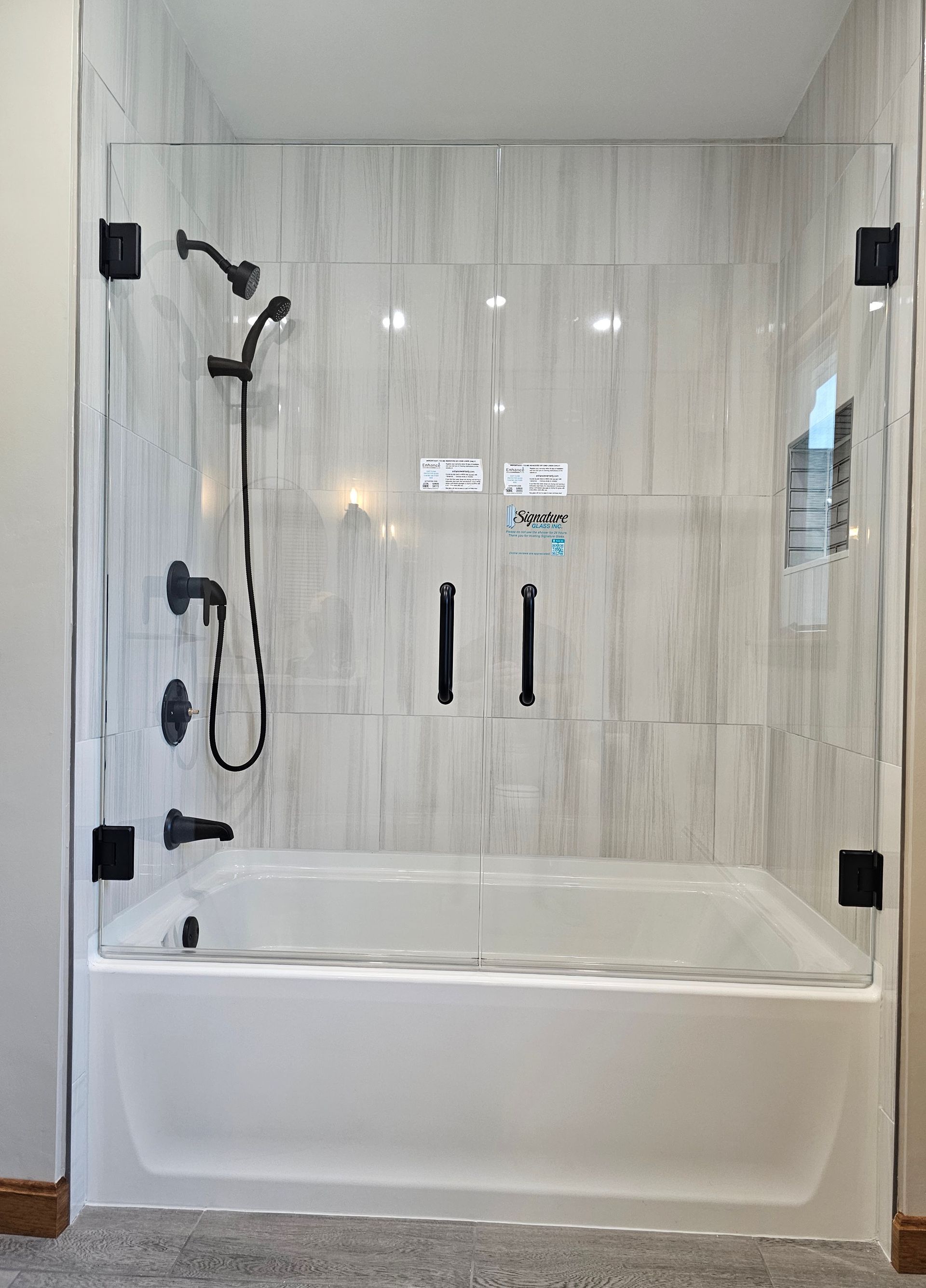 Shower enclosure with black hardware, glass doors, and a white bathtub.