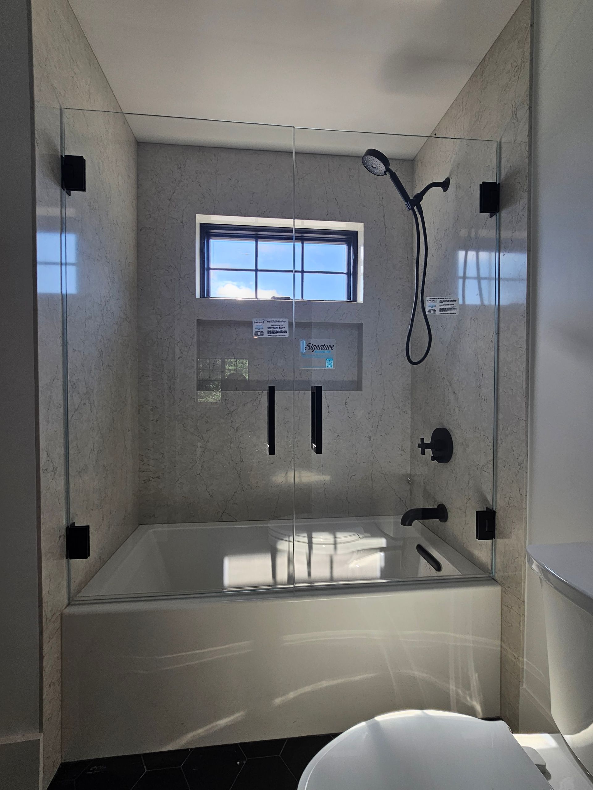Bathroom with a white tub, glass shower doors, black fixtures, and a window.