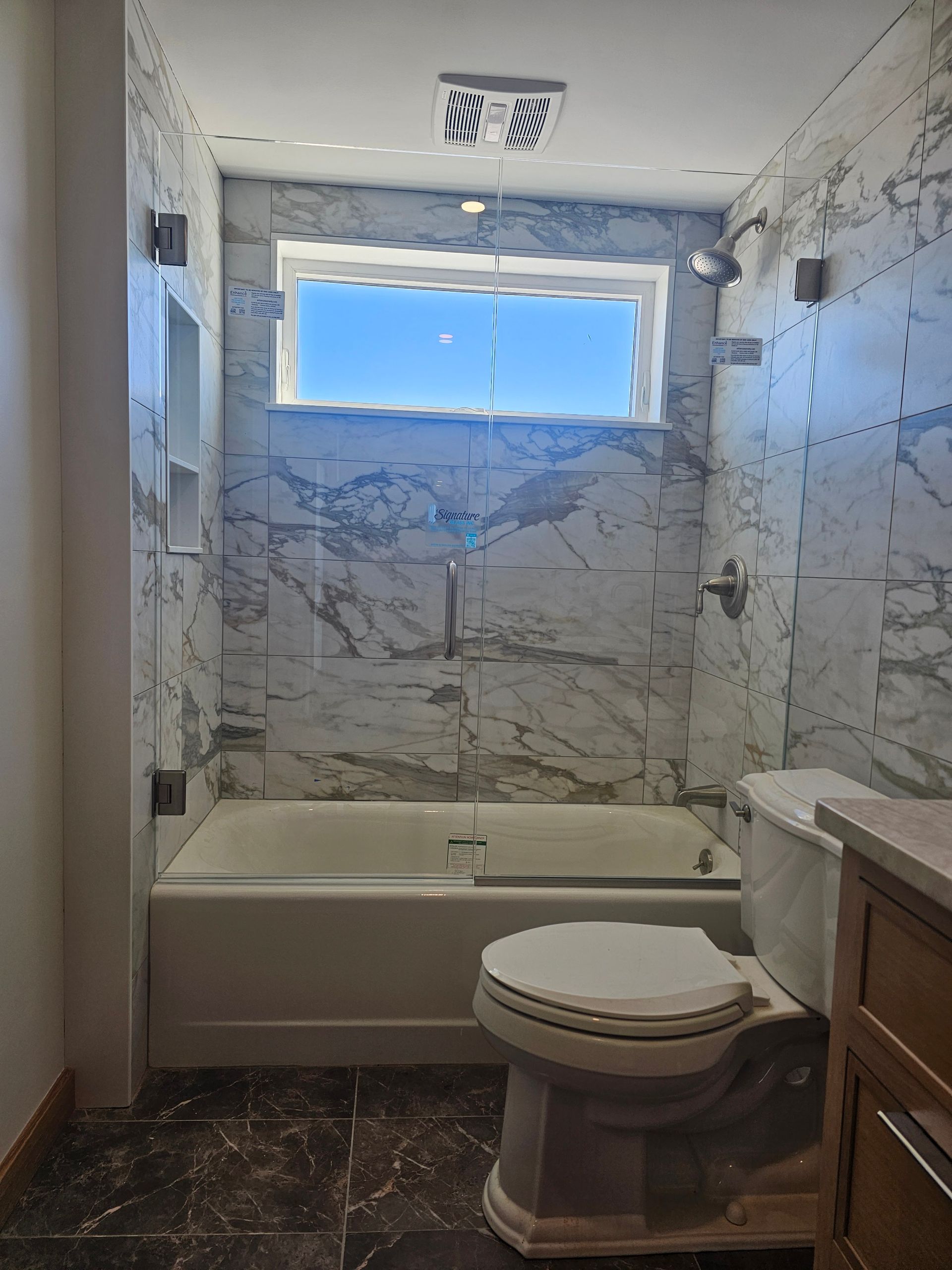 Bathroom with white marble tile shower walls, bathtub, toilet, and window.