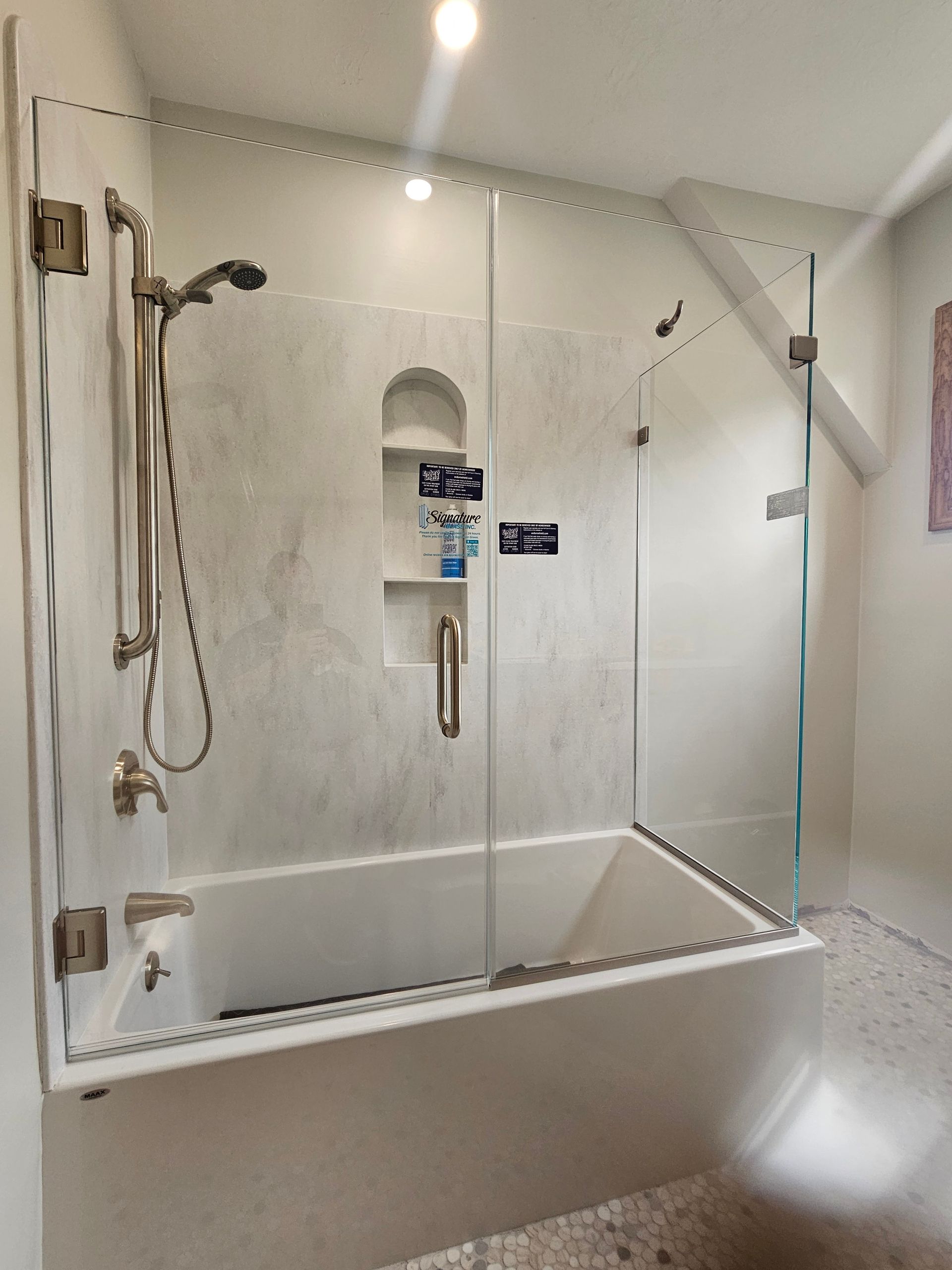 Bathroom with a white tub, glass shower doors, and gray tiled walls.
