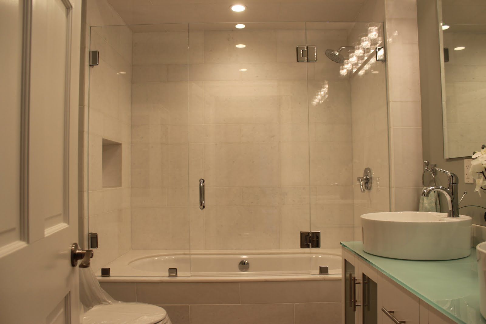 Bathroom with white tiling, a glass shower door, and a round sink.