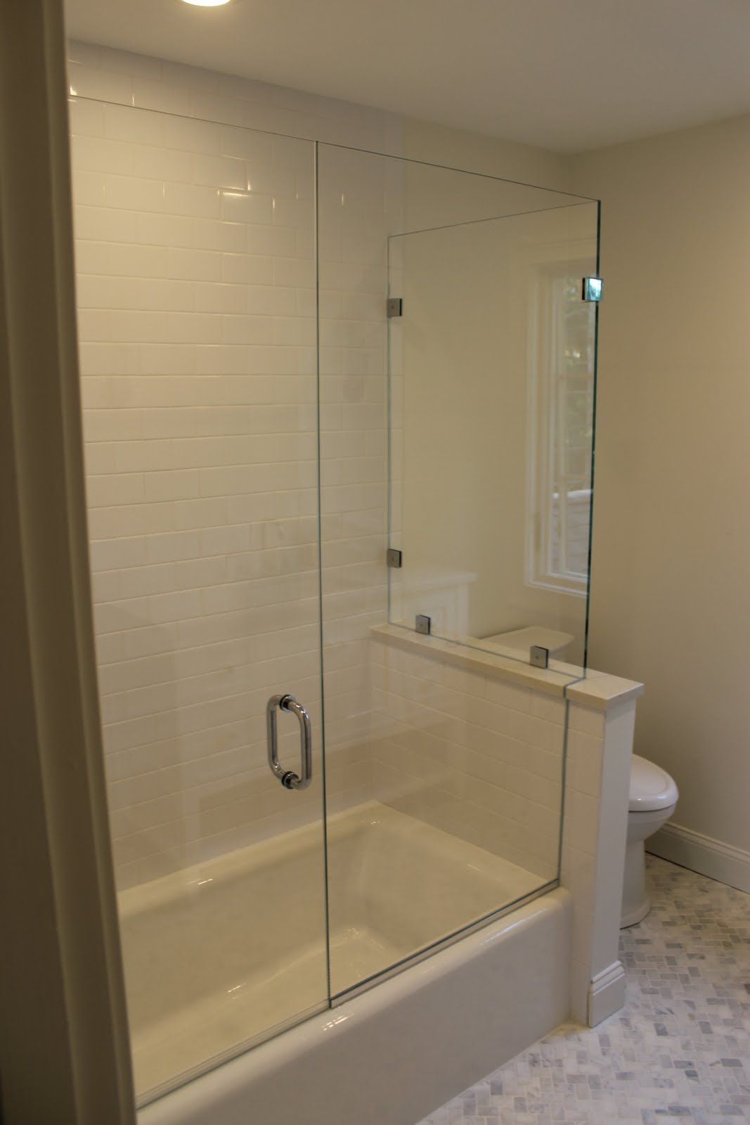 Glass shower enclosure with white tile and tub.
