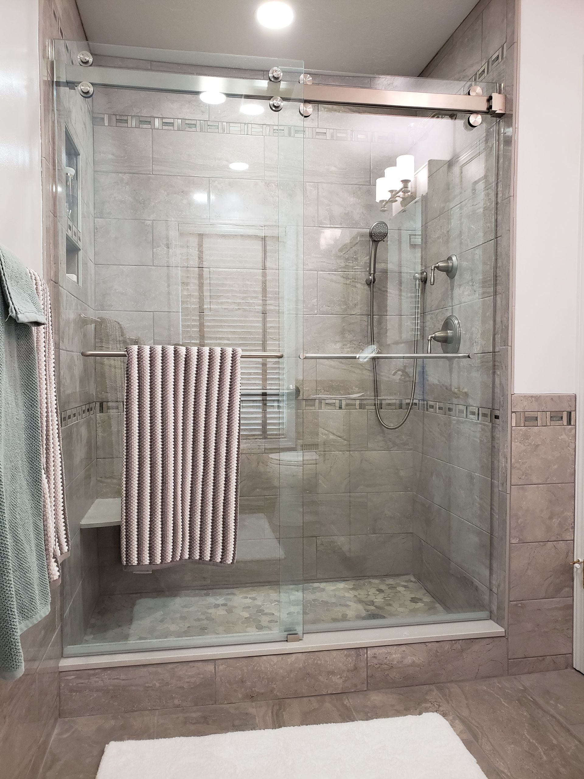 Shower with glass doors, tiled walls, towel rack, and a bench.