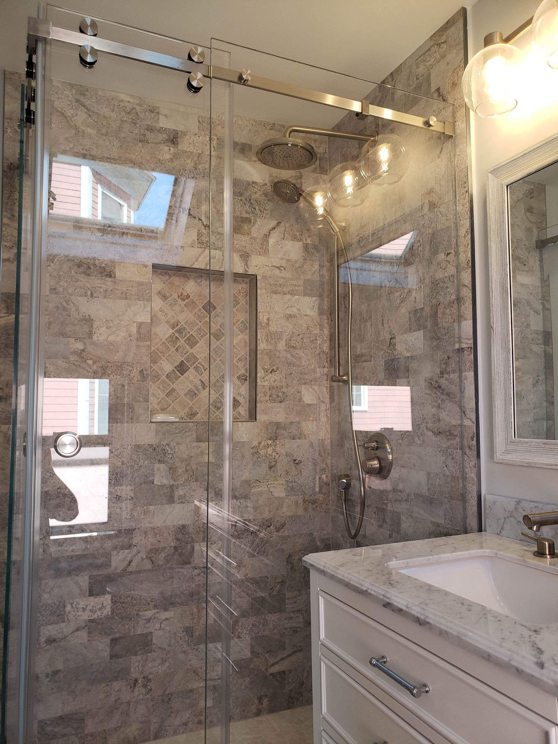 Shower stall with sliding glass doors, stone tile walls, built-in shelves, and a modern vanity.