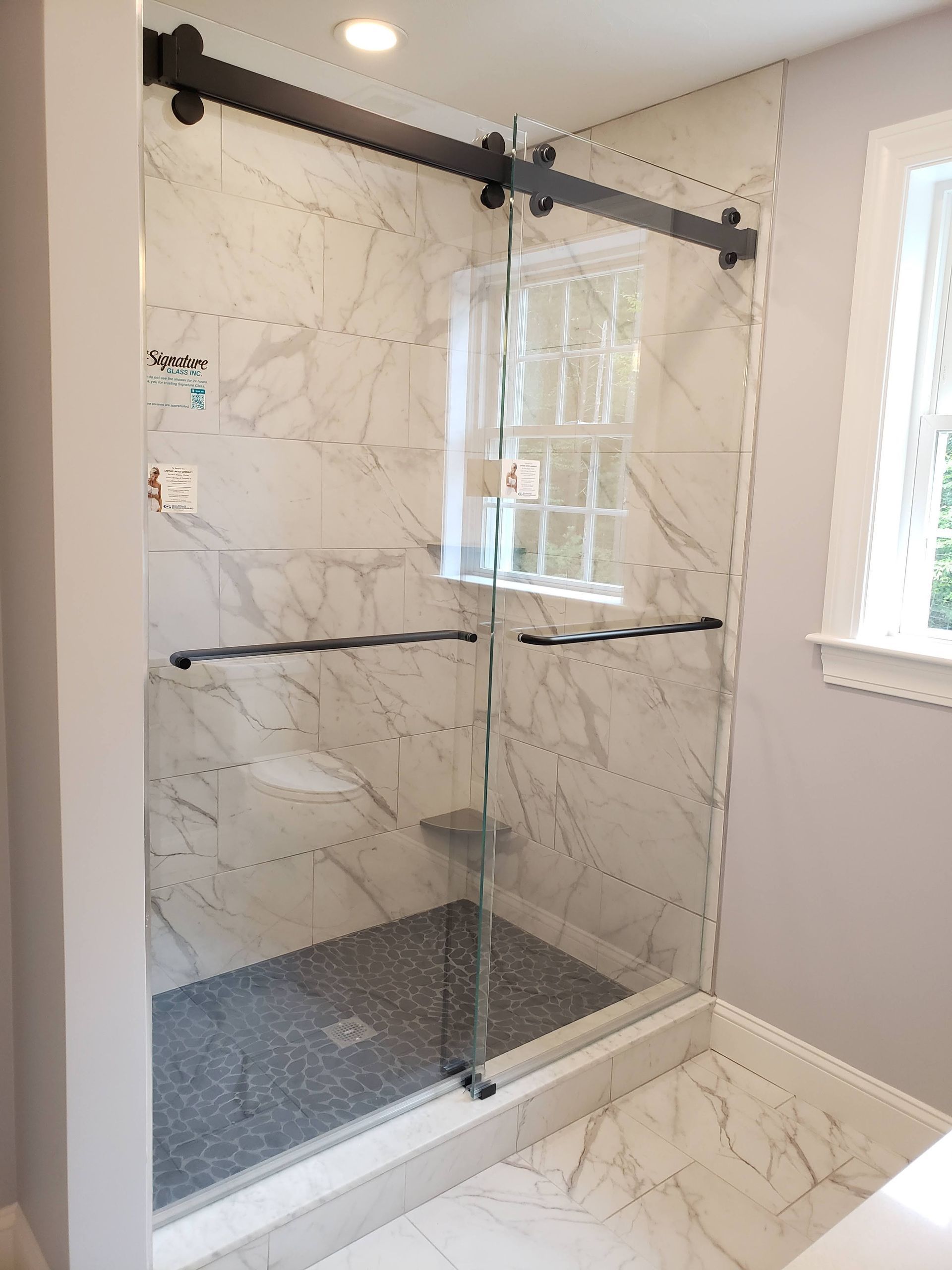 Shower with marble-look tile, dark sliding door hardware, and small window.