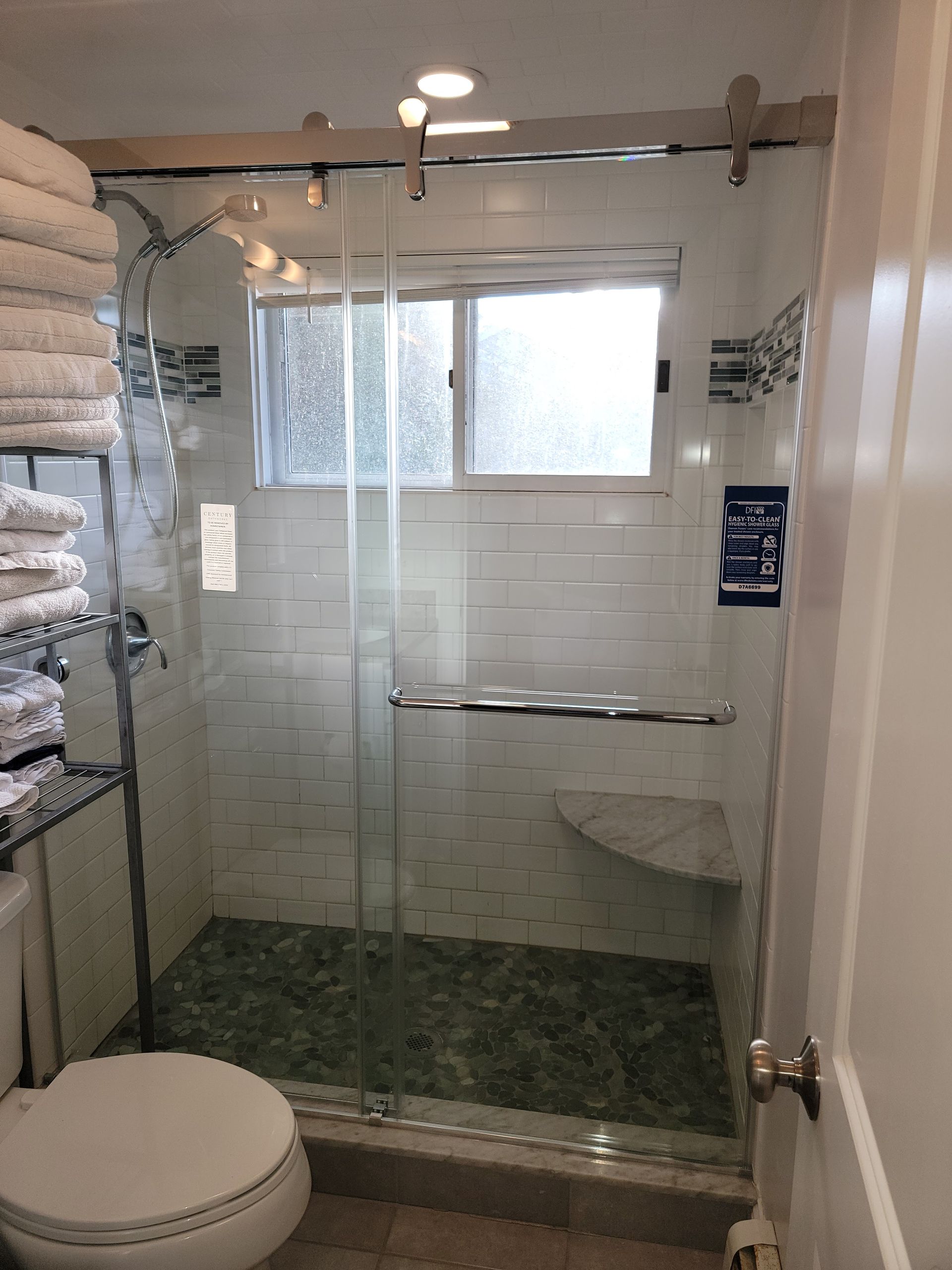 Bathroom with glass shower, white subway tile walls, stone floor, and a small window.