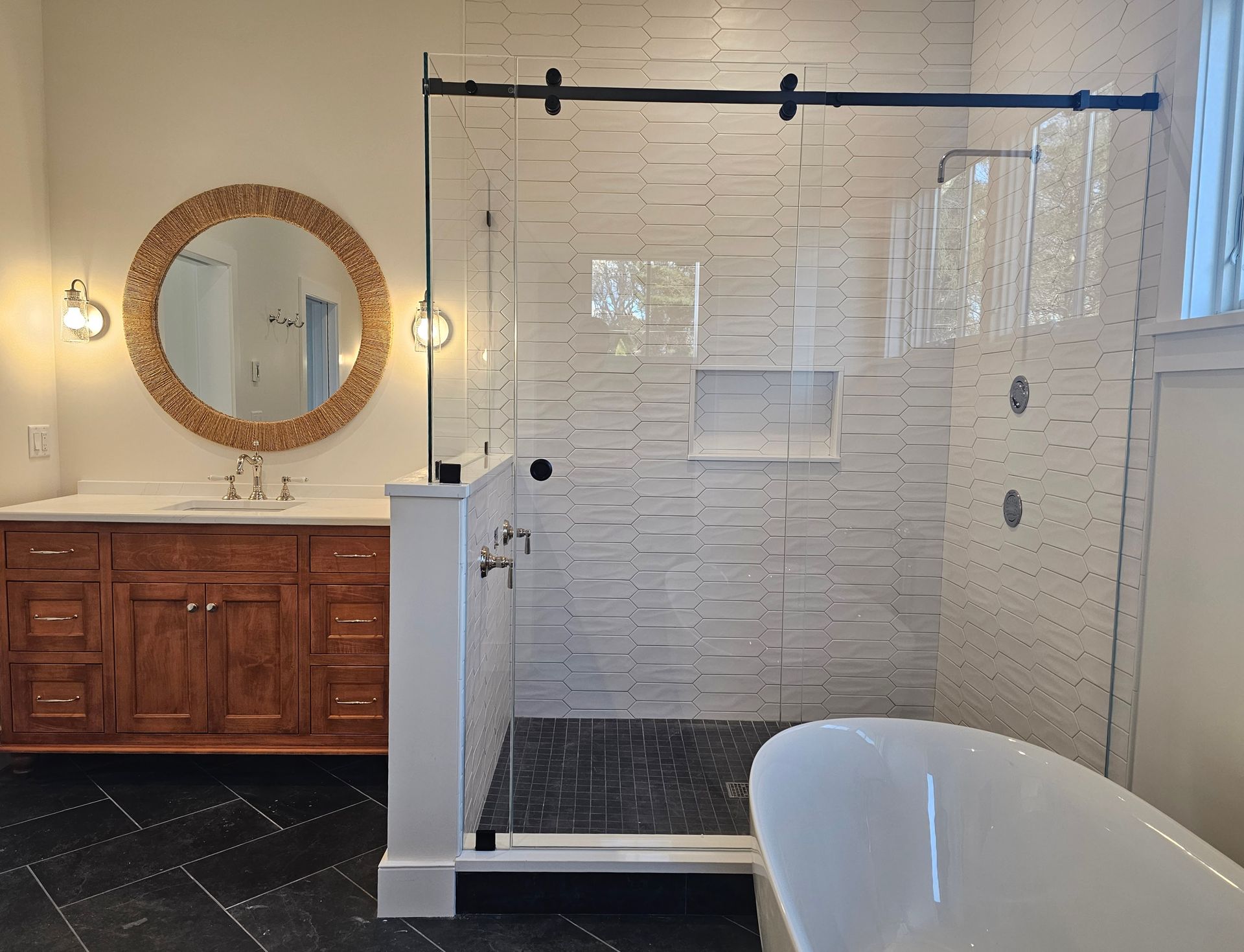 Bathroom with a walk-in shower, vanity, round mirror, and a clawfoot tub. The walls are white textured tile.