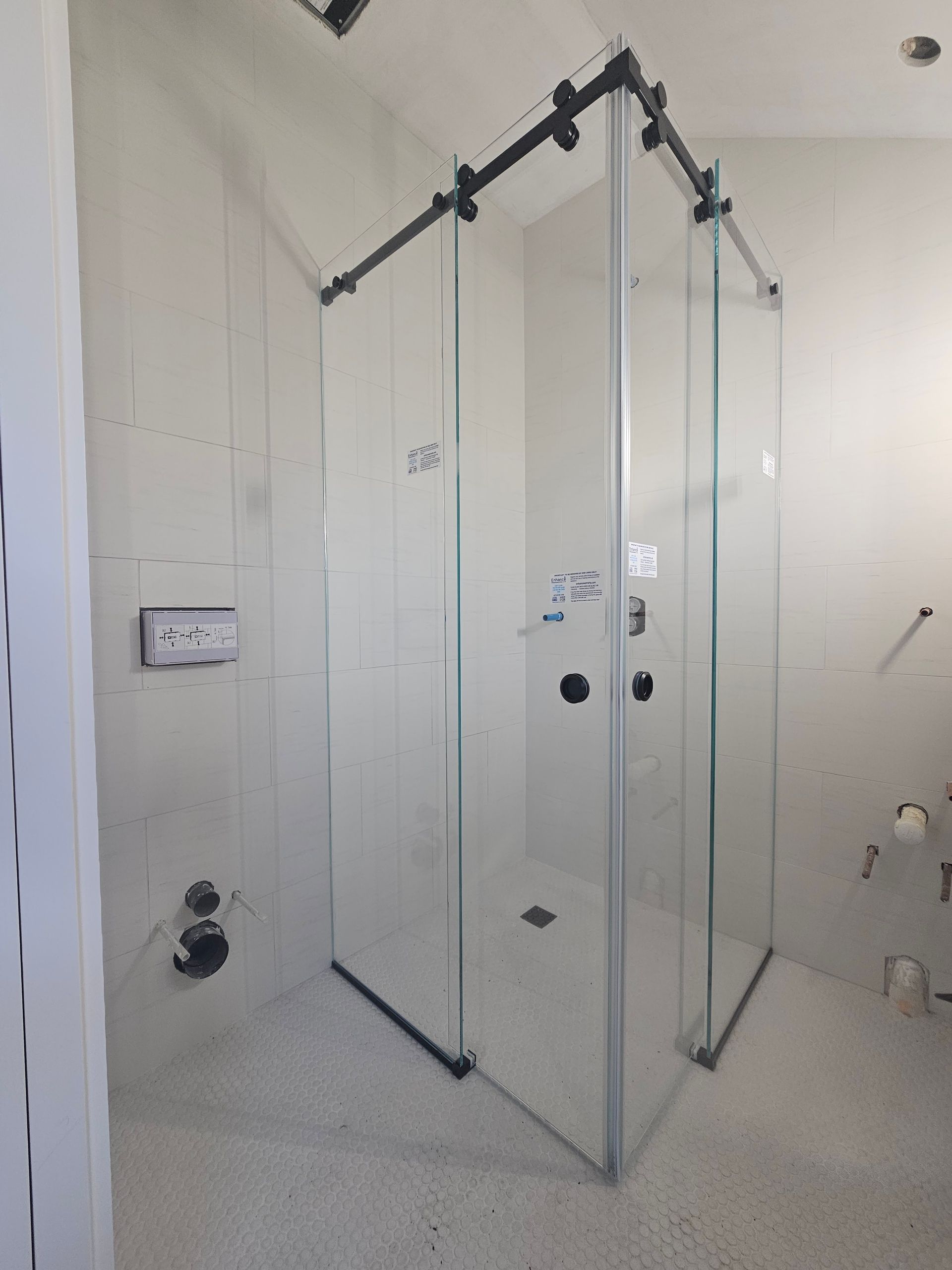 Clear glass shower enclosure being installed in a bathroom. Black track, gray walls, and unfinished floor.