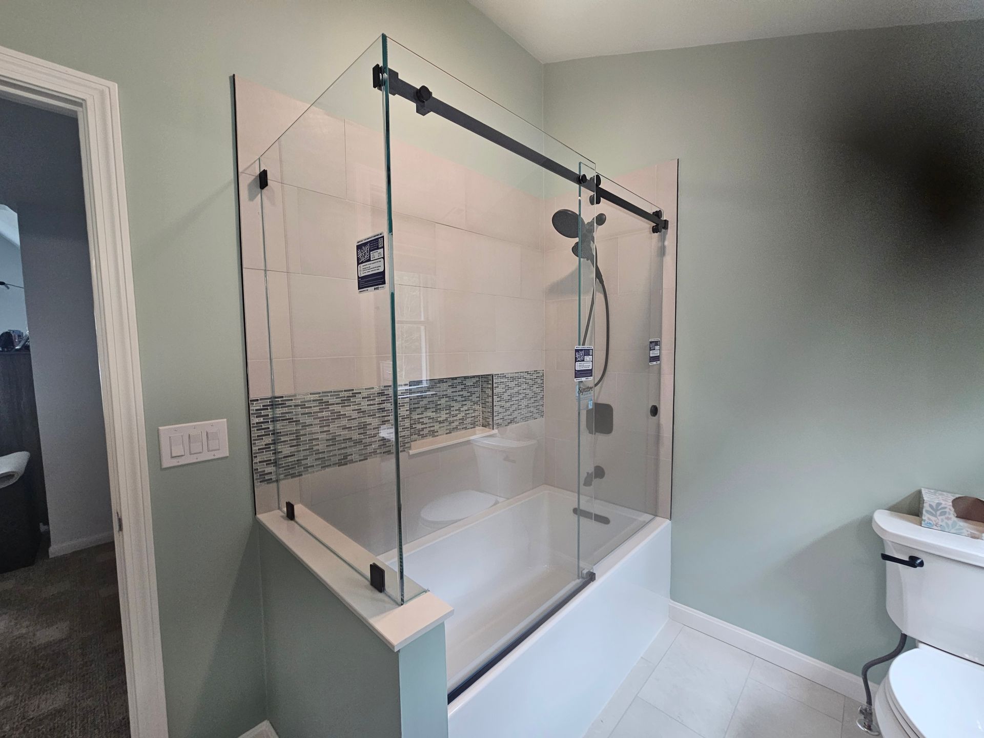 A modern bathroom with a glass shower enclosure over a white bathtub. Light green walls, white tile floor.
