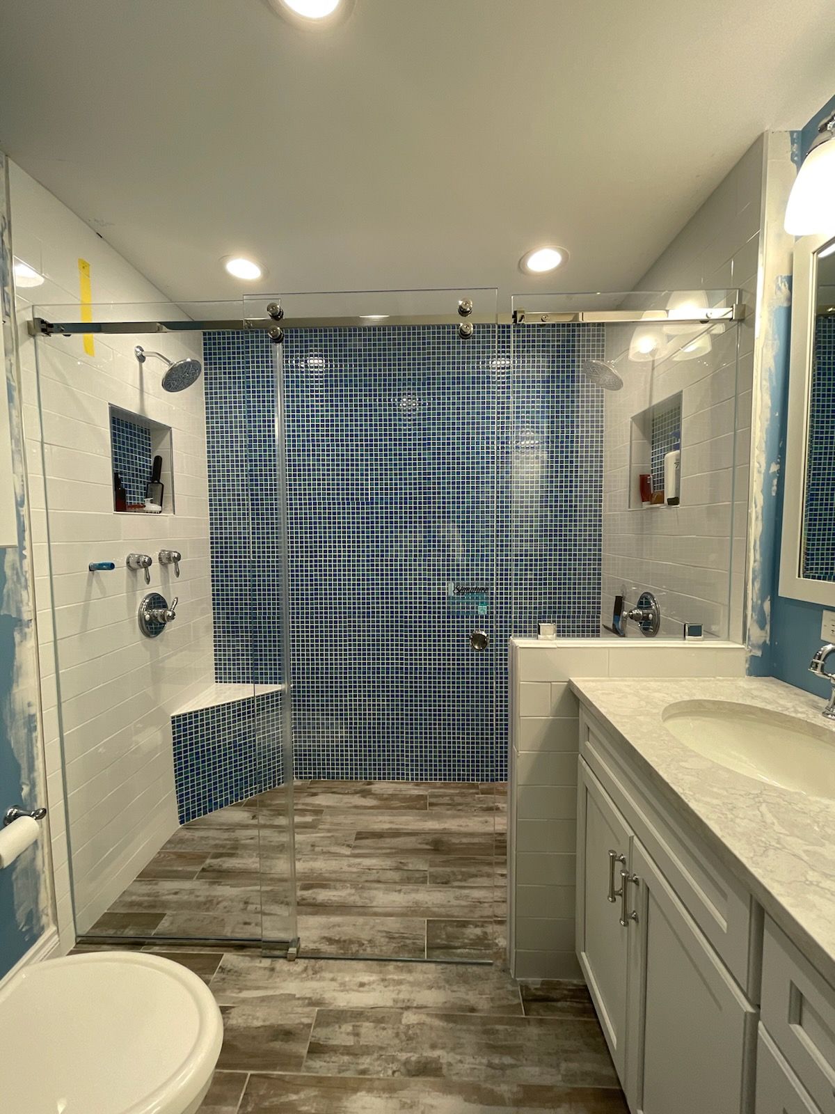 Bathroom with shower and vanity. Blue and white tile, glass shower doors, wood-look floor.