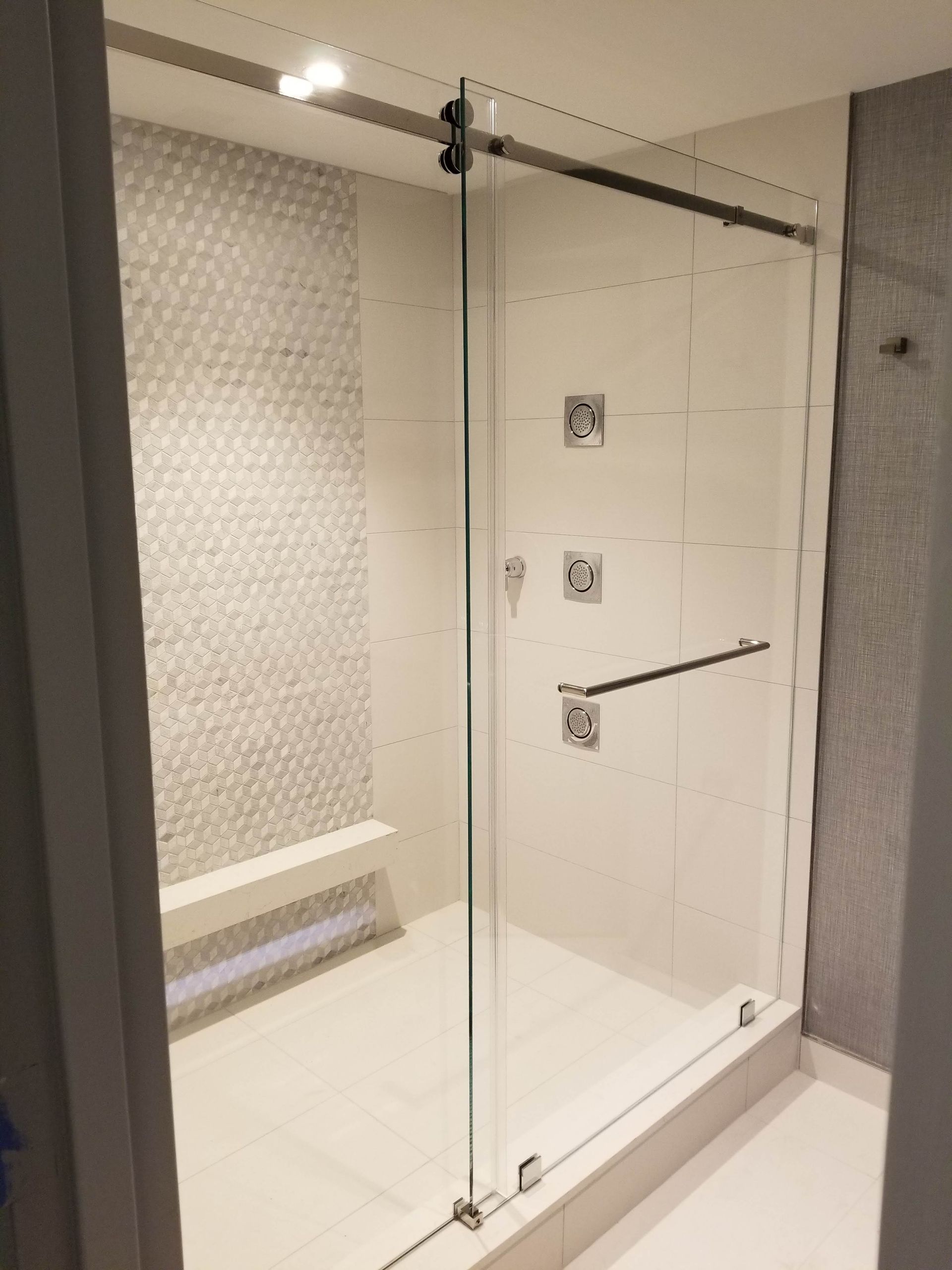 Modern glass shower with sliding door, white tile walls, and a built-in bench.