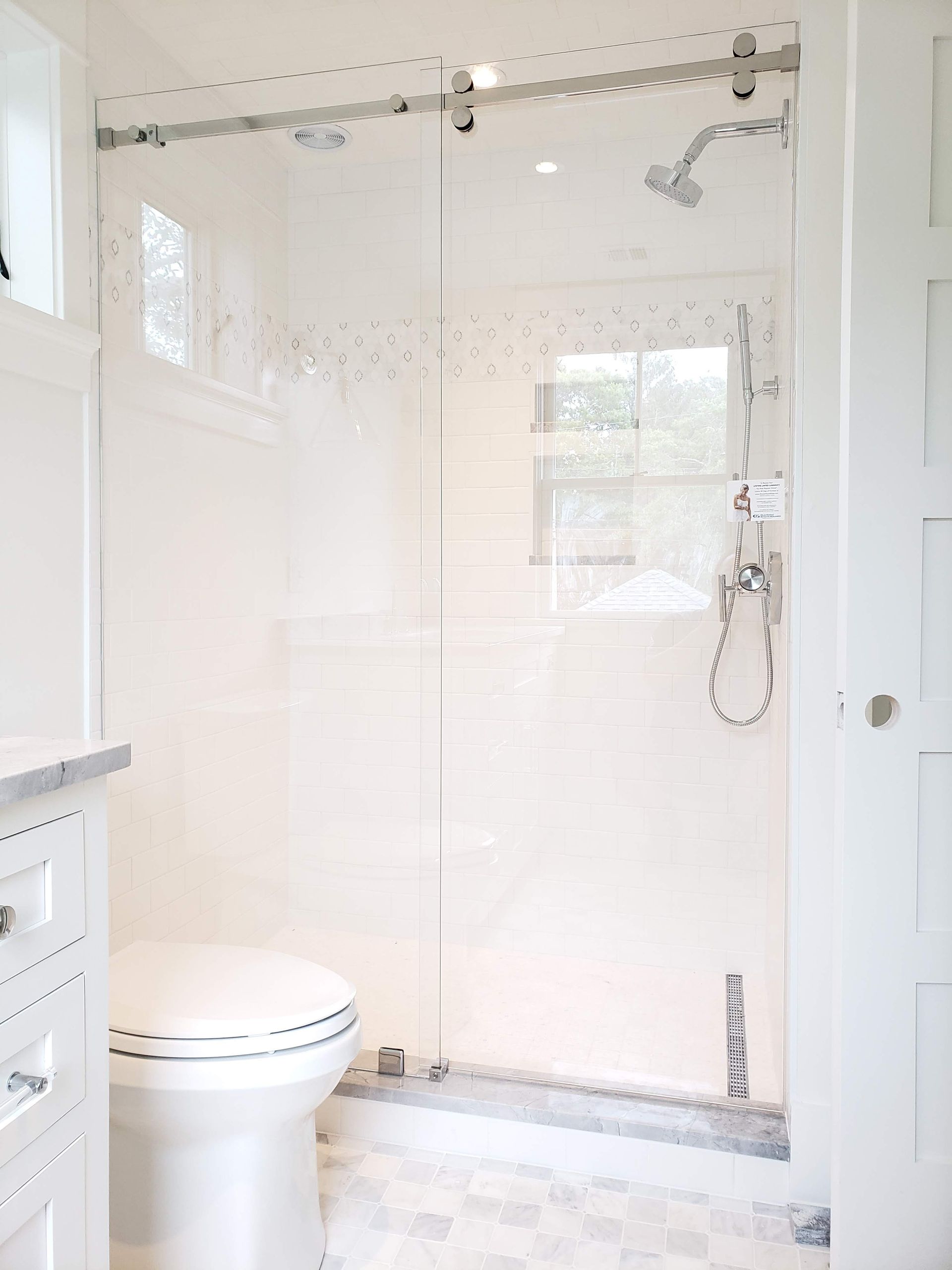 Bright white bathroom with glass shower door, toilet, and marble floor.