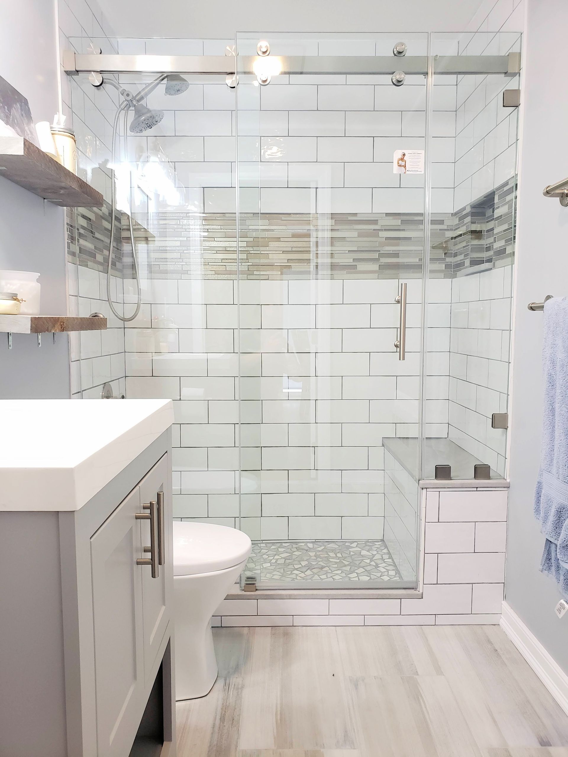 Modern bathroom with glass shower, subway tile, floating shelves, and gray vanity.
