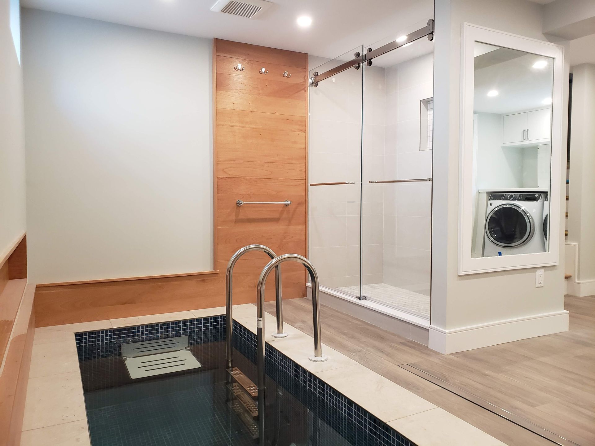 Indoor spa area with a small pool, shower, and laundry area.  Light wood and white finishes.