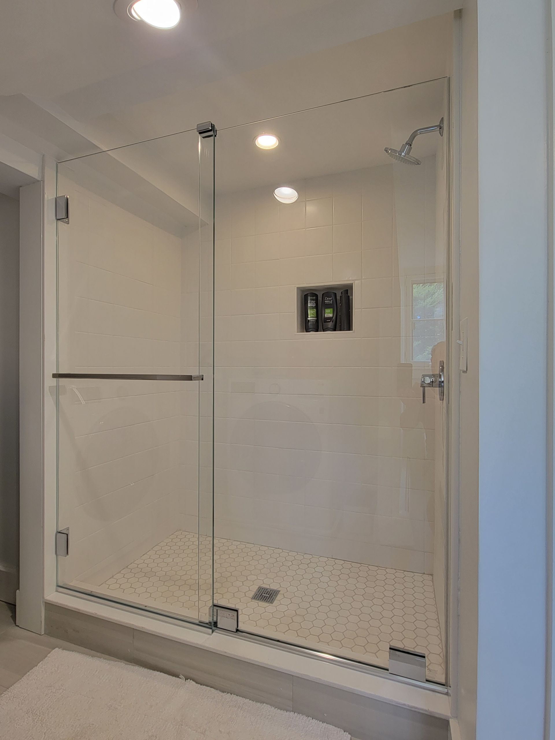 Glass shower enclosure with white tile walls and pebbled floor. Chrome fixtures.