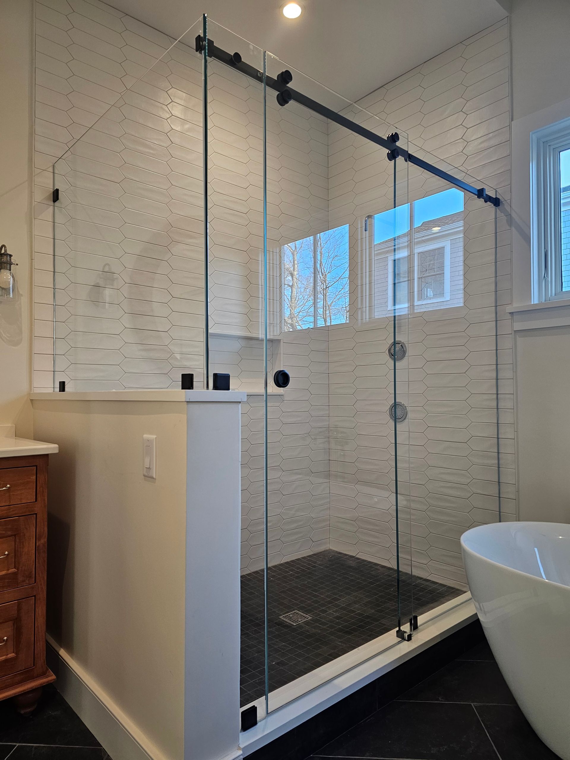 Modern bathroom with glass shower enclosure, black trim, and white walls.
