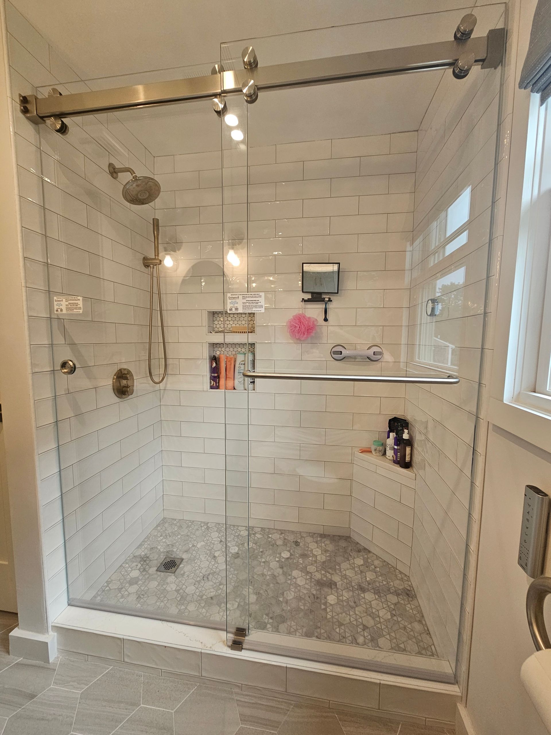 Glass shower with white tile walls and a gray stone floor. Silver hardware.