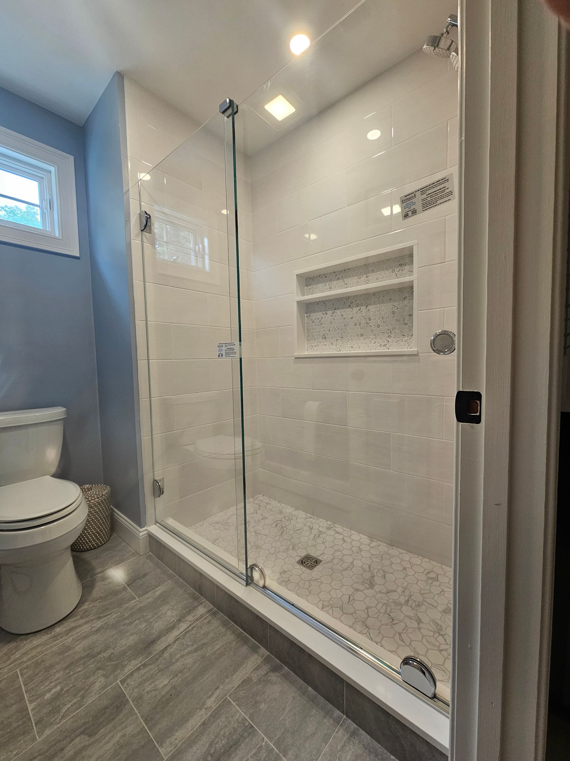 Modern bathroom with glass shower doors, white tile, and gray flooring.