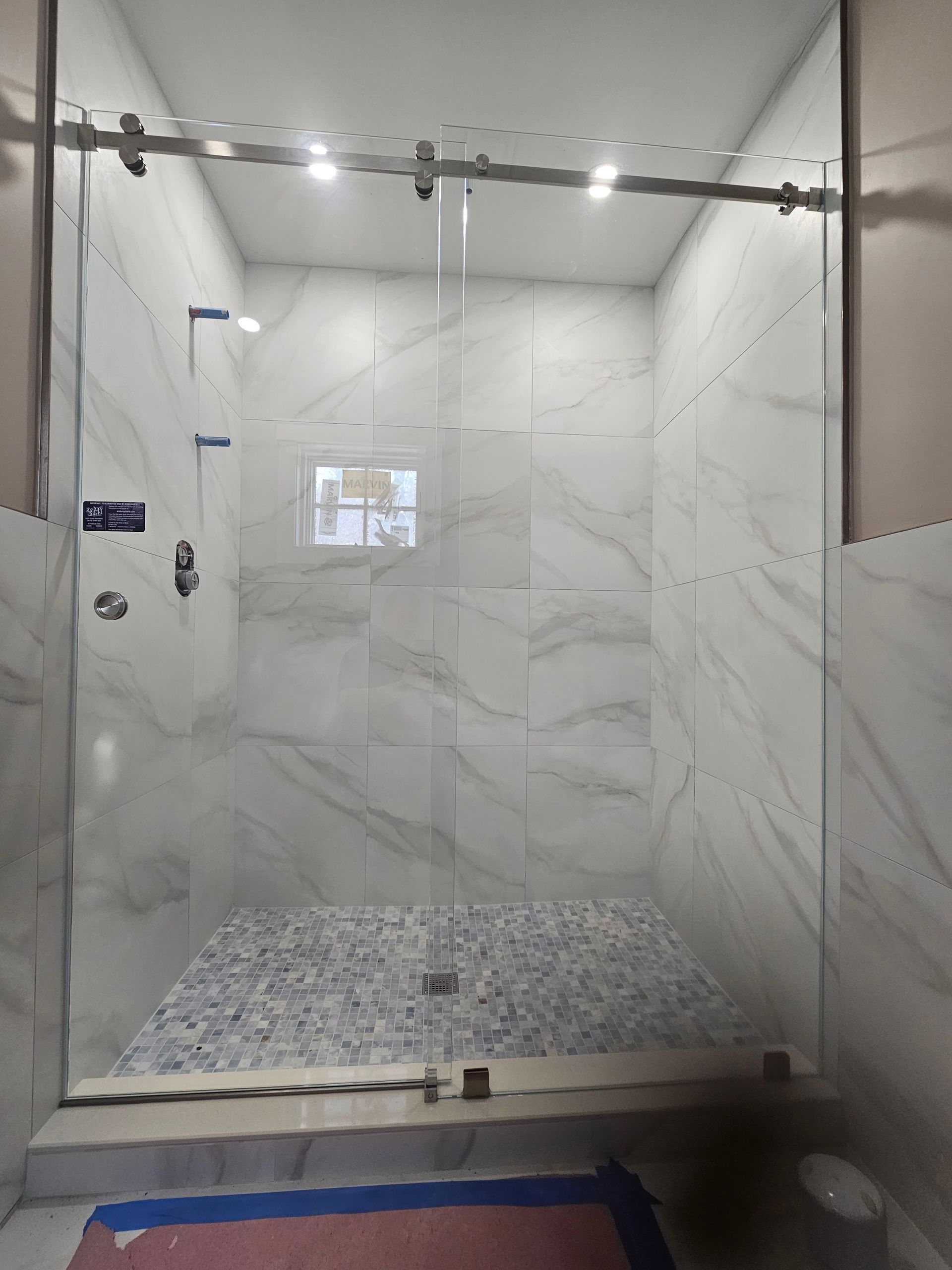 Glass shower enclosure with white marble-look tile walls and a mosaic tile shower floor. Sliding door.