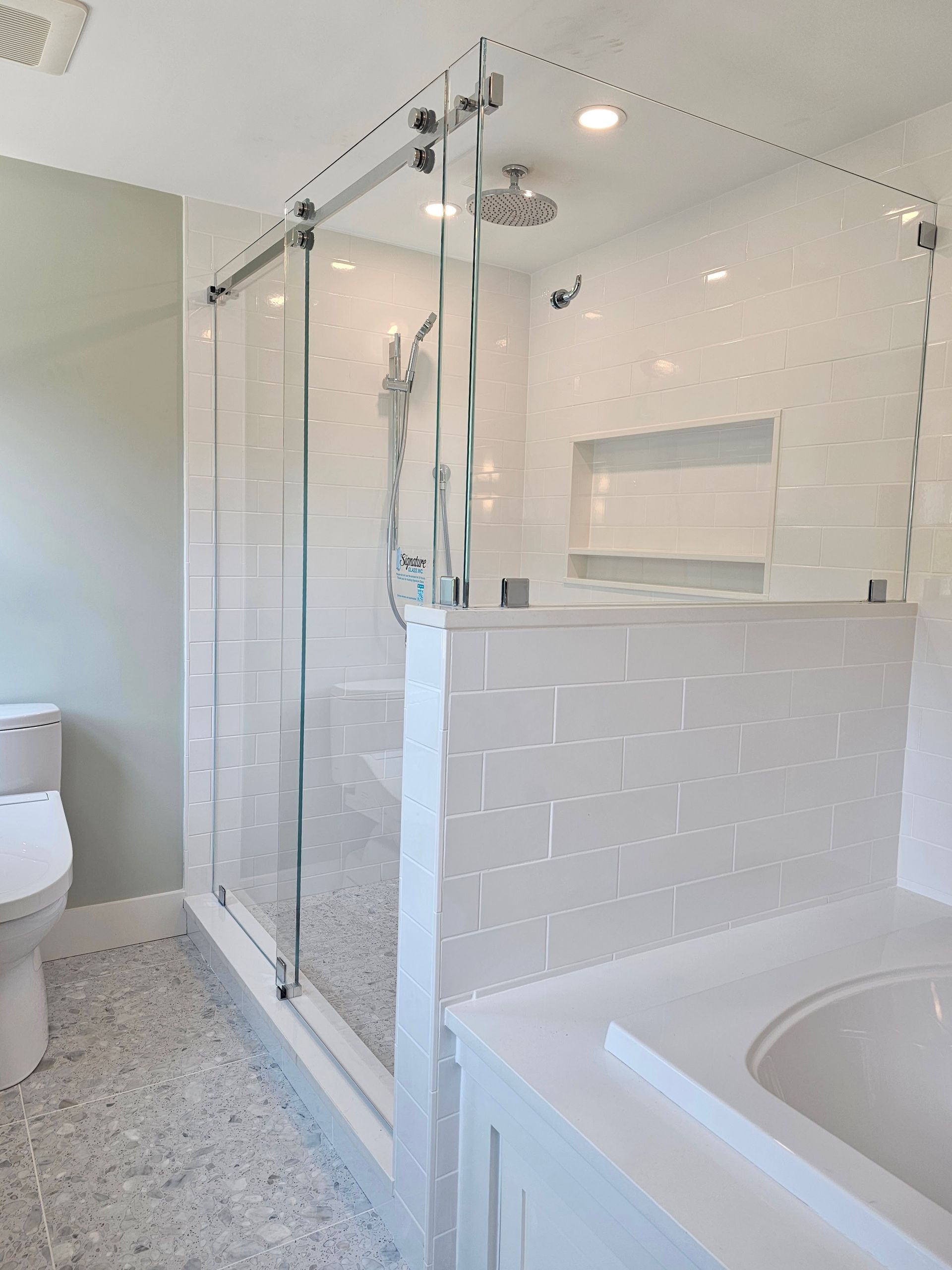 Modern bathroom with glass shower enclosure, white tile, and a built-in shelf.