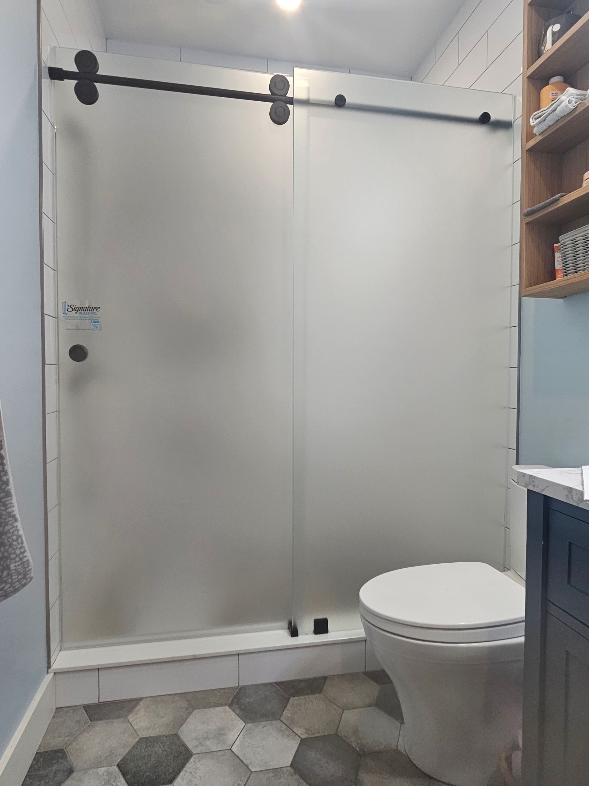 Bathroom with frosted glass sliding shower door, white toilet, and hexagon tile floor.