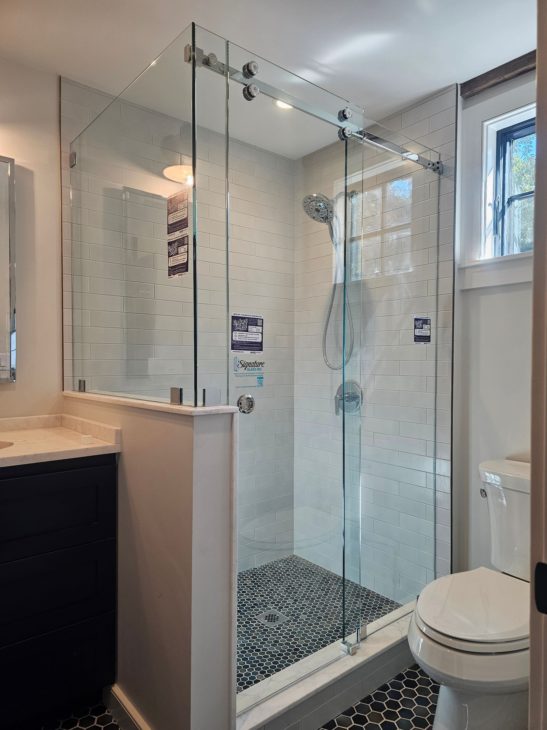 Glass shower enclosure with sliding door in a modern bathroom. Black and white tiled floor, white walls.