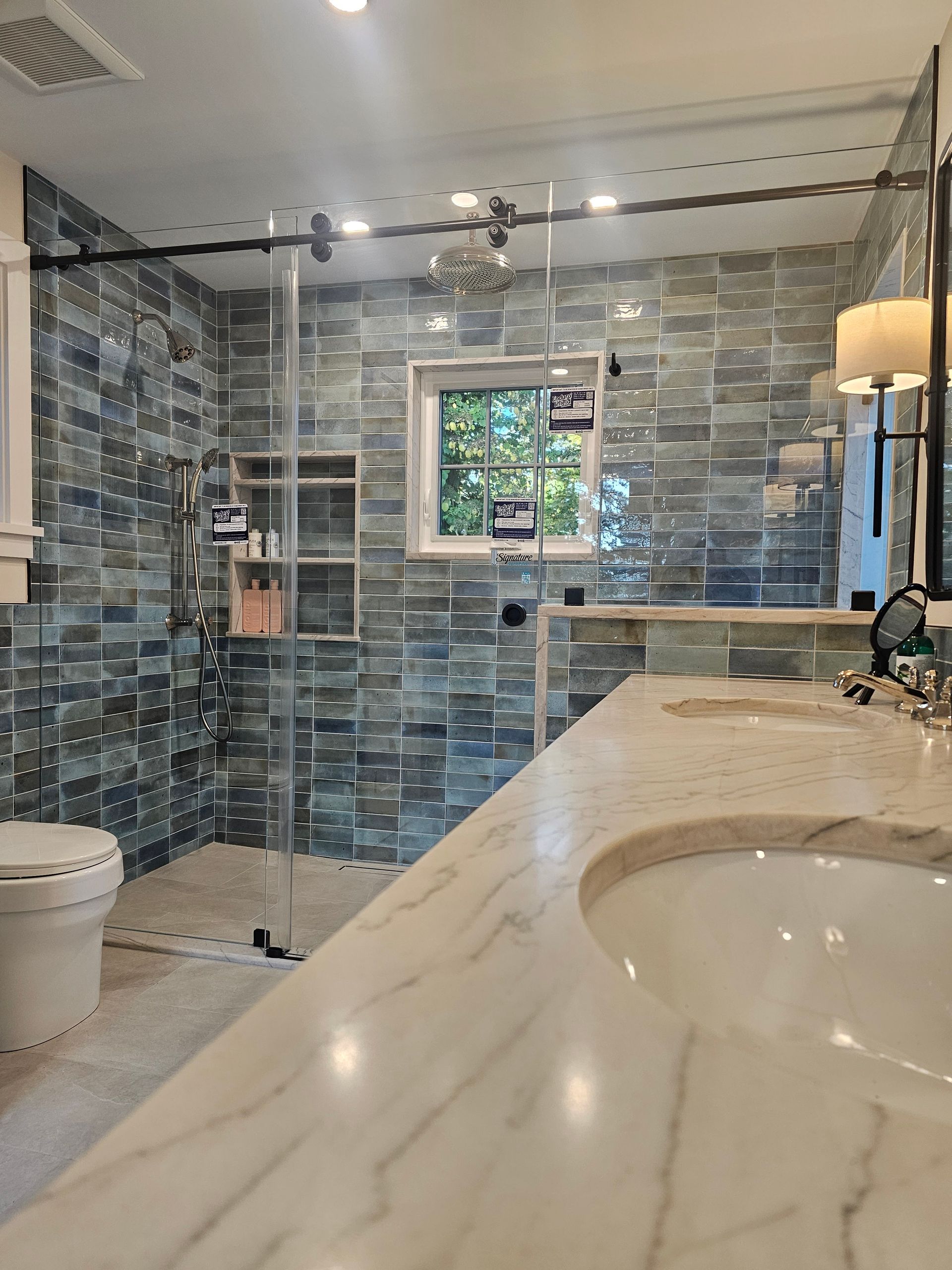 Modern bathroom with blue tile shower, glass enclosure, white countertop with sink, and toilet.
