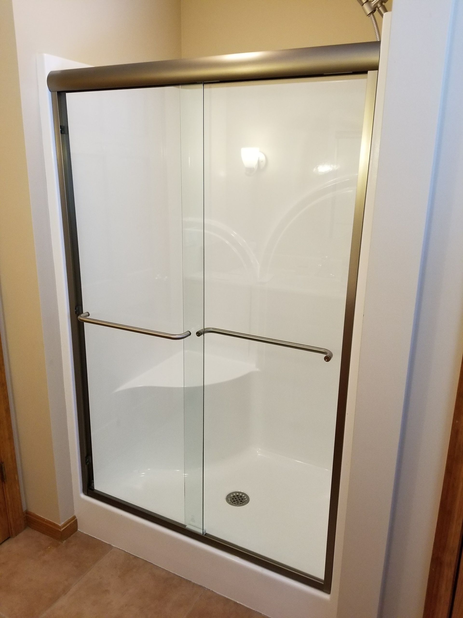 White shower stall with sliding glass doors and grab bars; bronze trim.