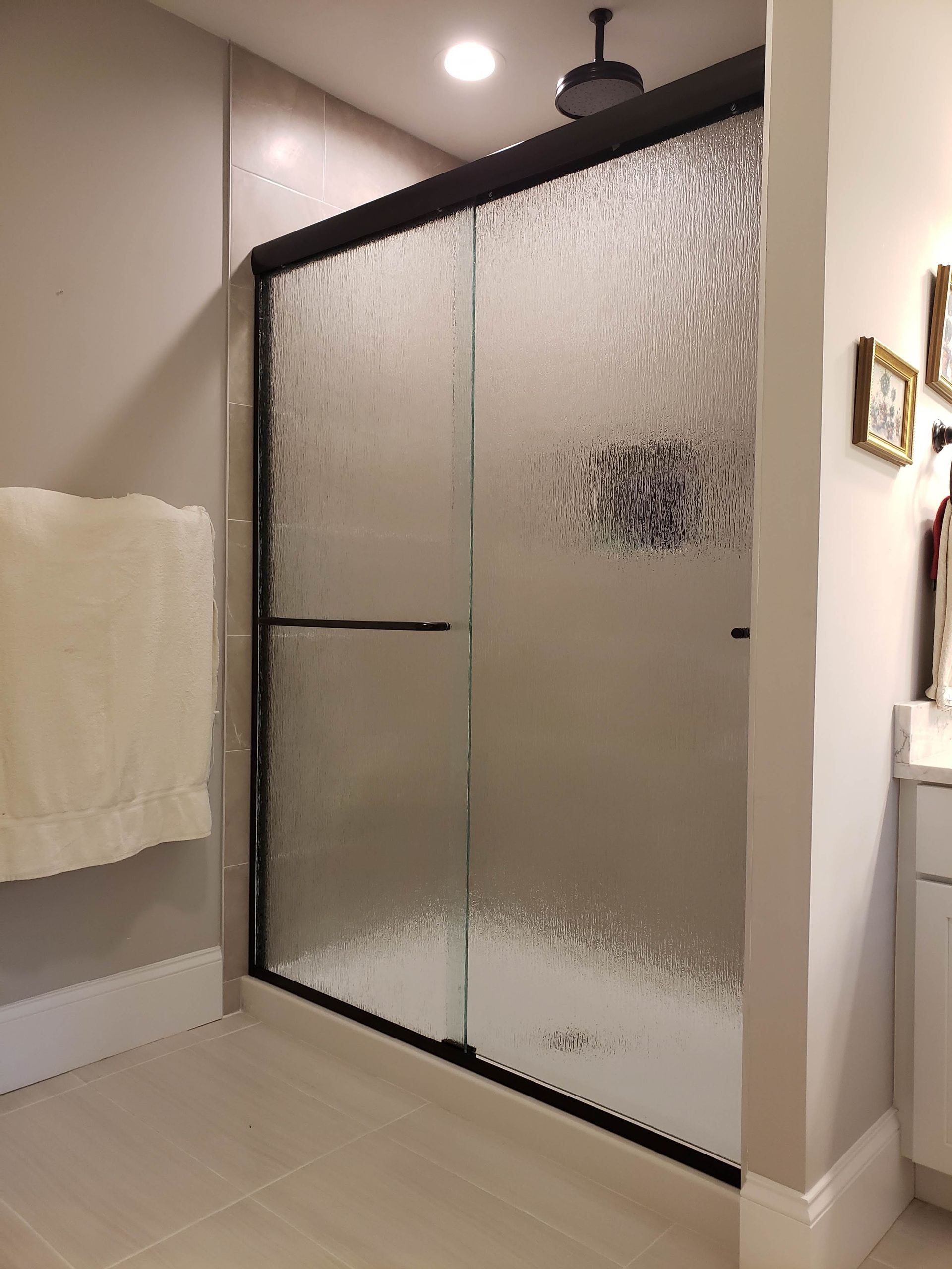 Shower enclosure with textured glass, black frame, and a rain showerhead.