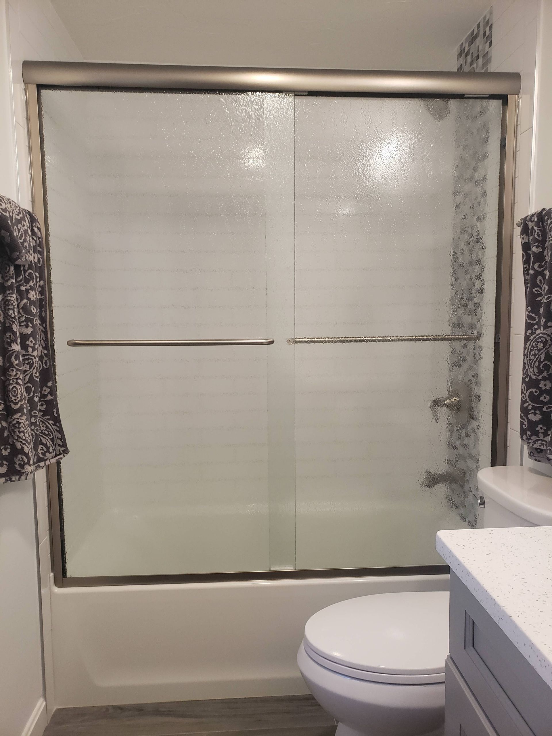Bathroom with glass shower doors, white toilet, and gray cabinets.