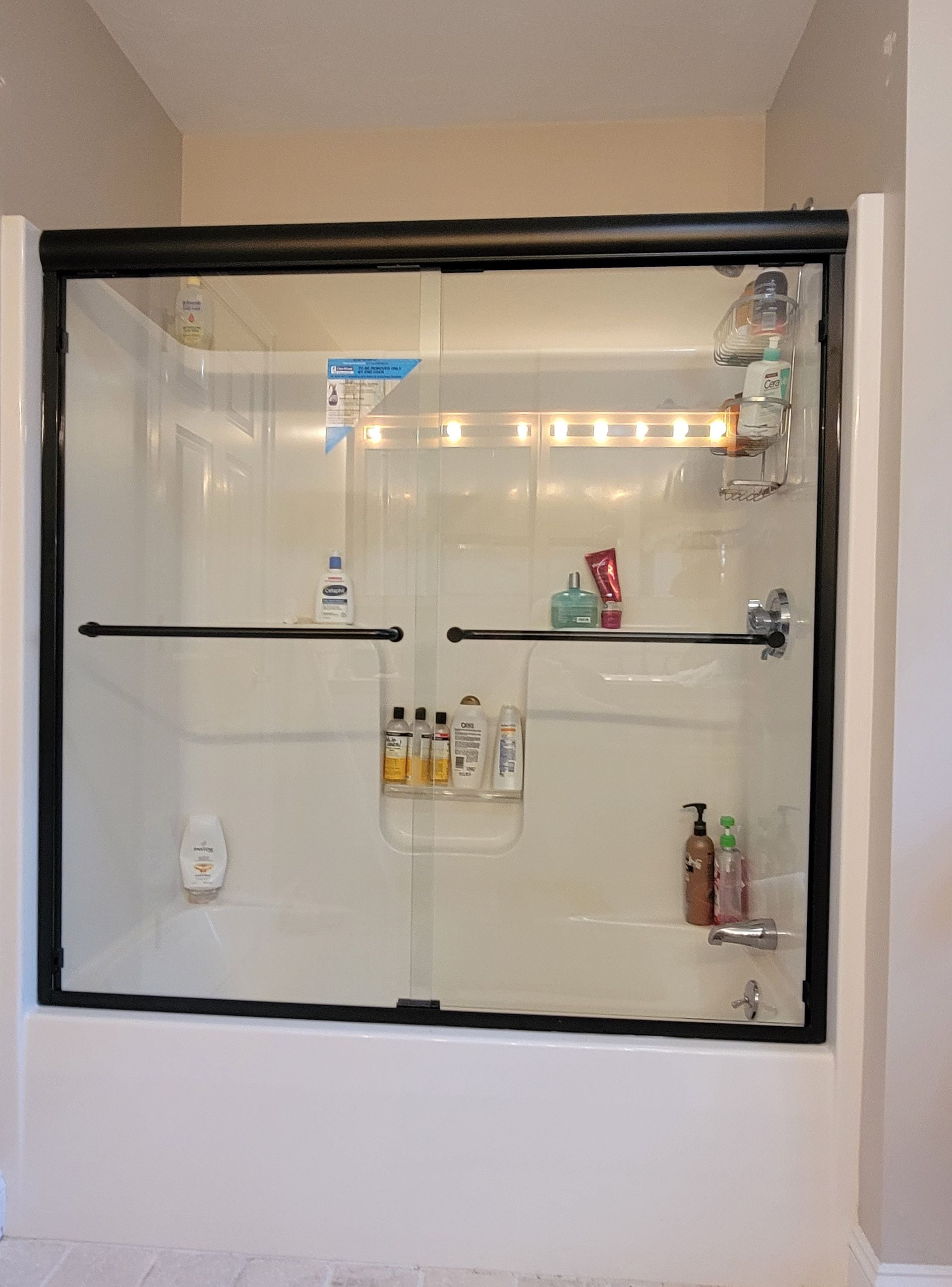 Shower stall with sliding glass doors, black frame. Shower products are visible inside the stall.