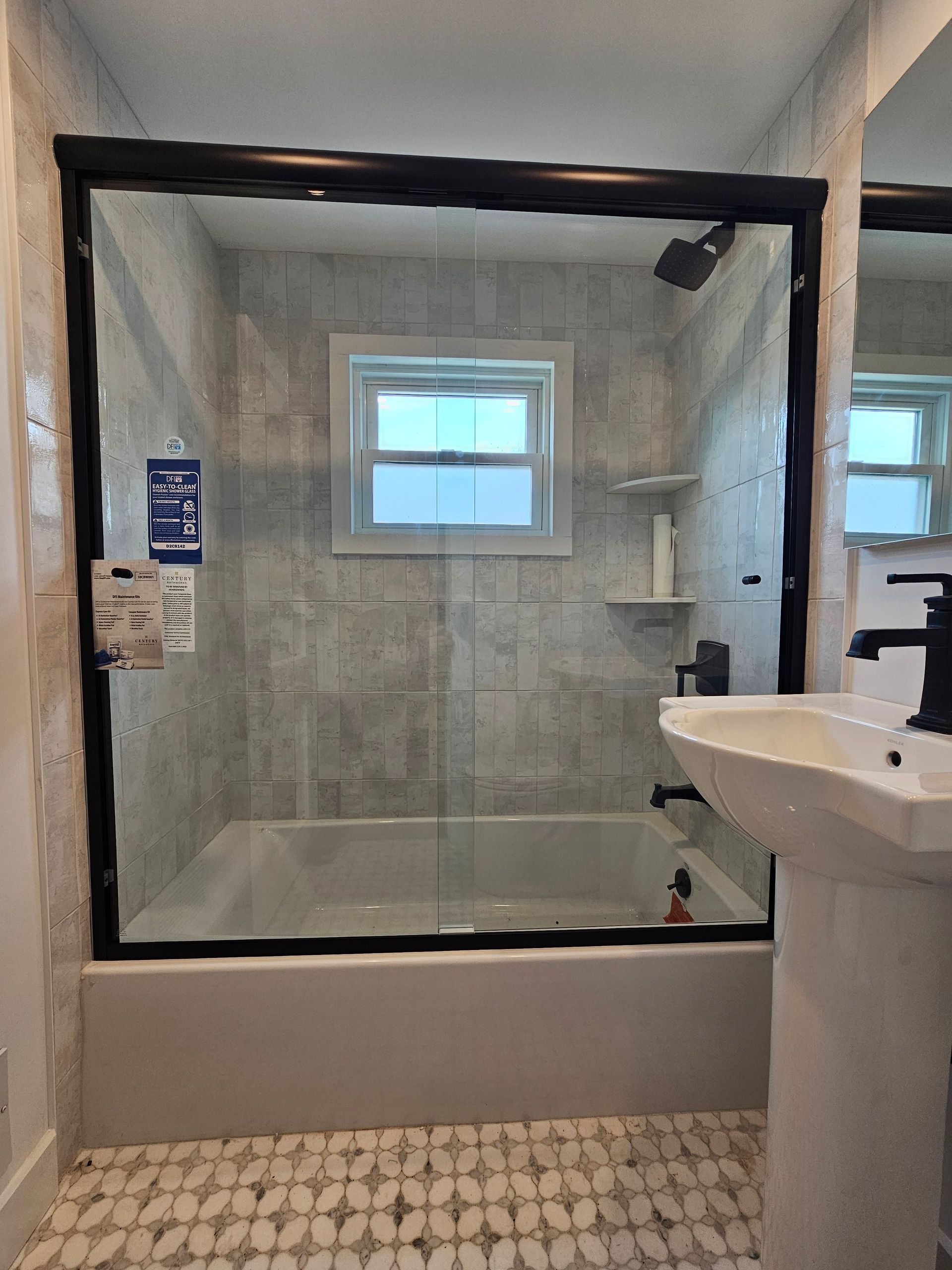 Bathroom with a bathtub, glass shower doors with black frames, and light gray tiled walls.