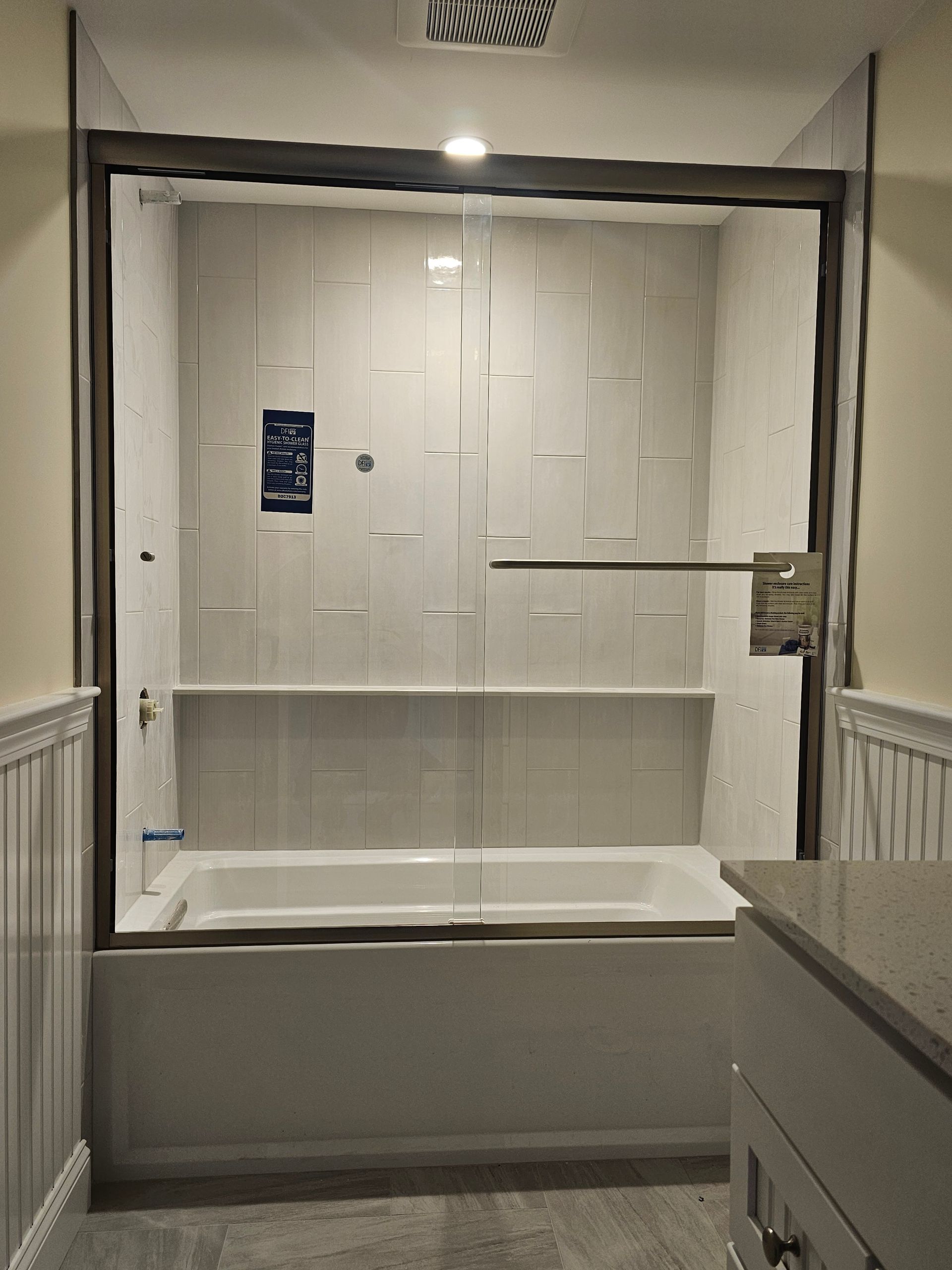 Bathroom with white tile walls, a bathtub, and a glass shower door.