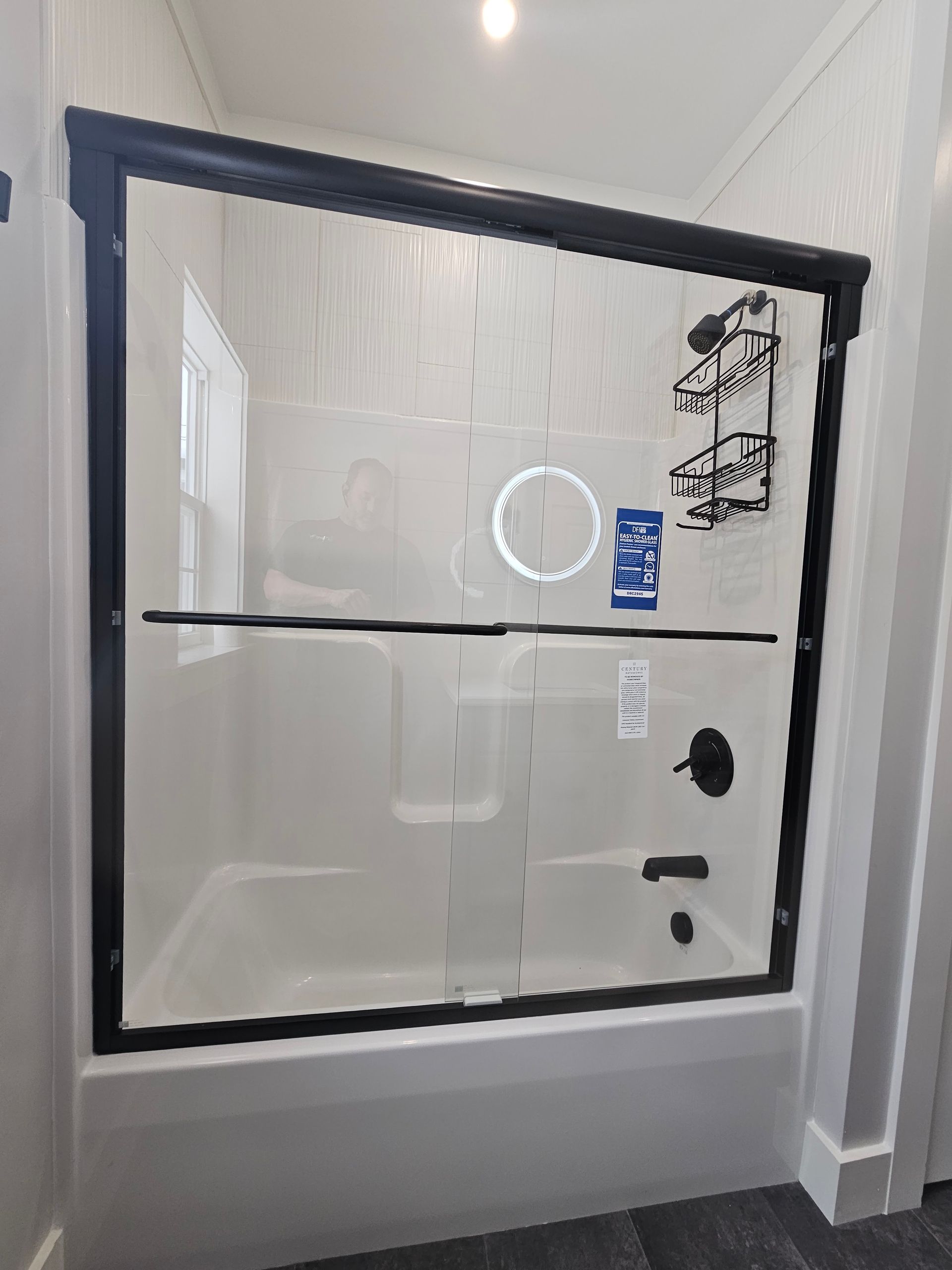 Black-framed sliding shower door on a white tub; black fixtures; white walls; window.