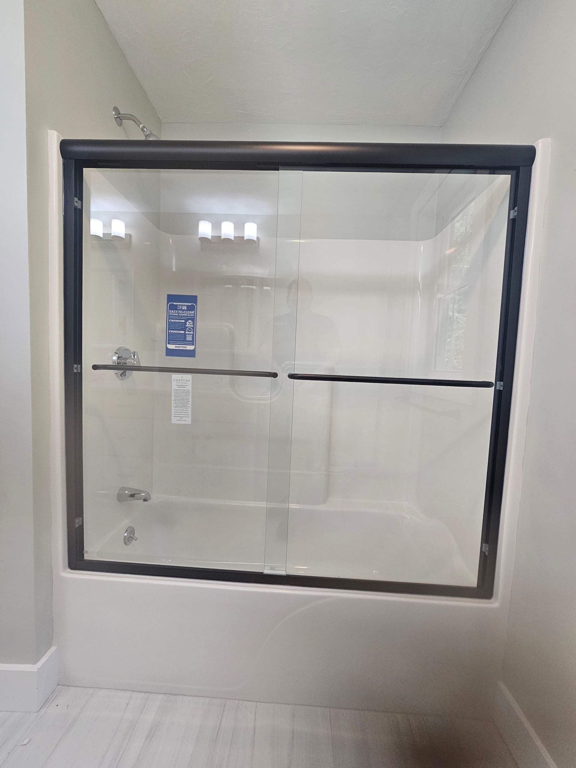 Shower with sliding glass doors, black frame, in a white-tiled bathroom.