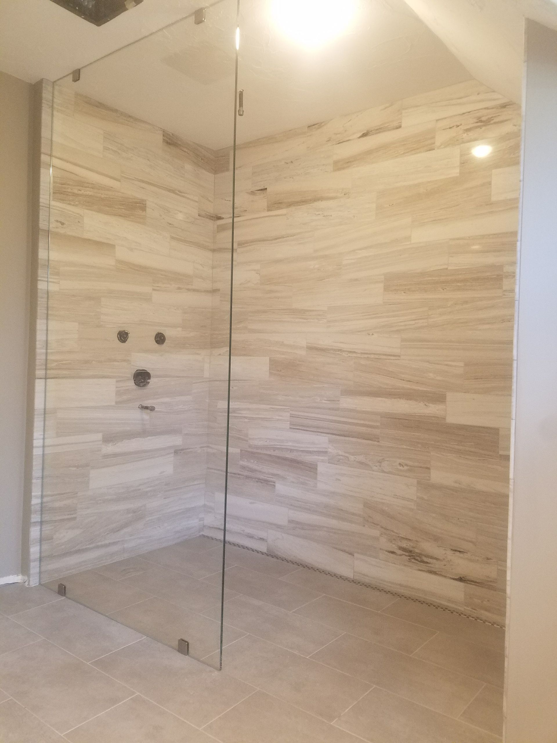 Glass-walled shower with light-colored tile walls and floor. The shower has a rain-head faucet.