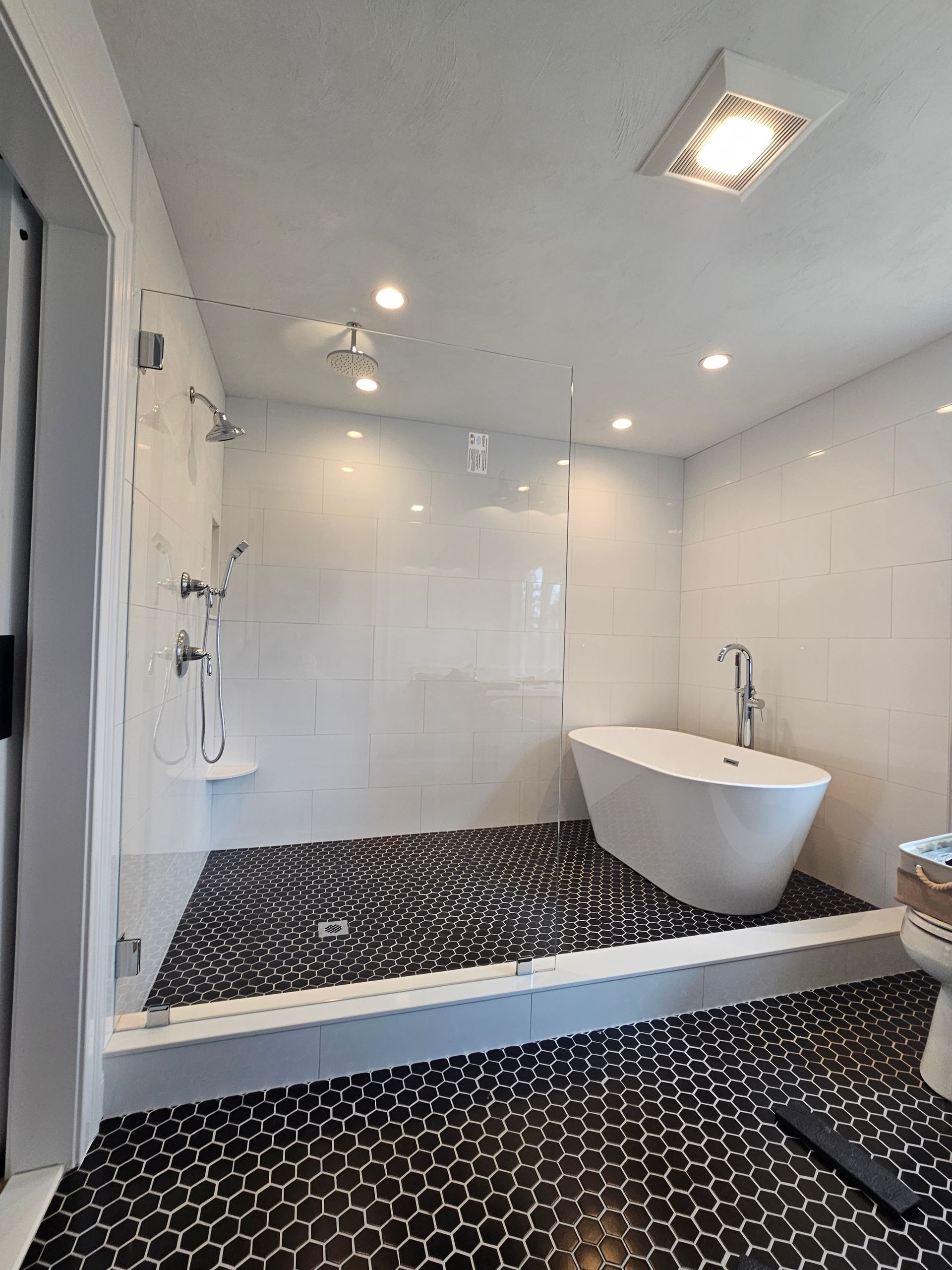 Modern bathroom with glass shower, freestanding tub, black pebble tile floor, and white walls.
