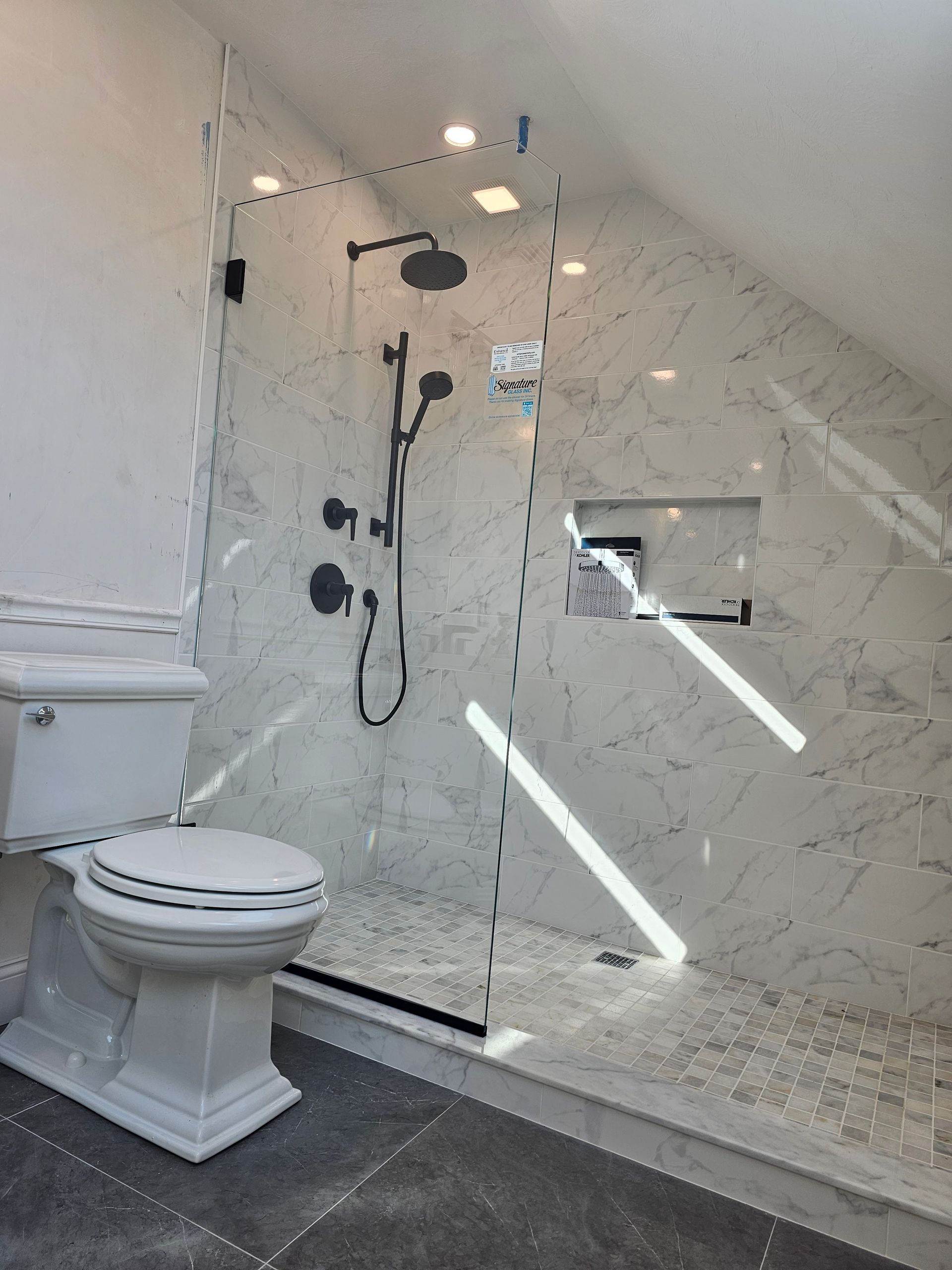 Modern bathroom with marble tile, glass shower, and toilet.