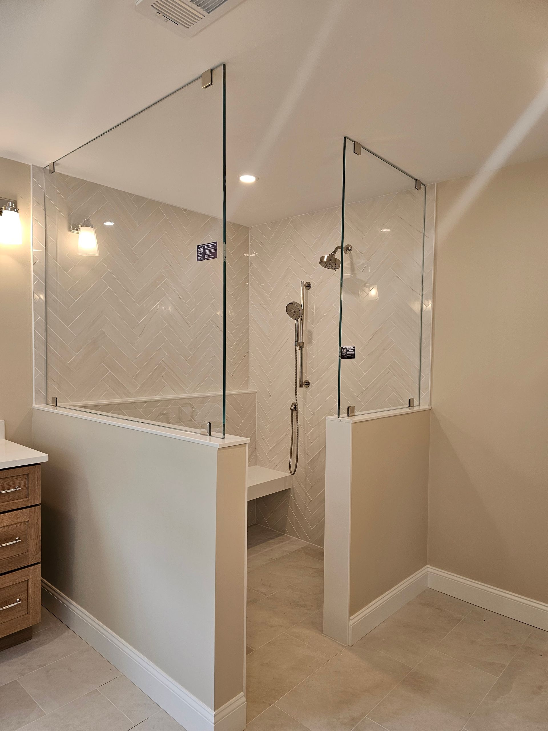 Bathroom with walk-in shower. Glass panels sit atop beige walls. White tile background with shower heads and bench.