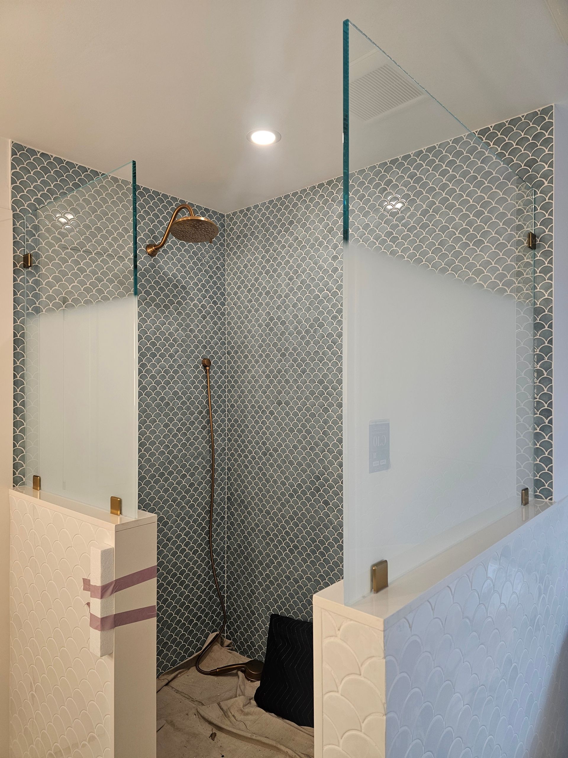Shower with three glass walls, gray tiled walls, and gold fixtures.