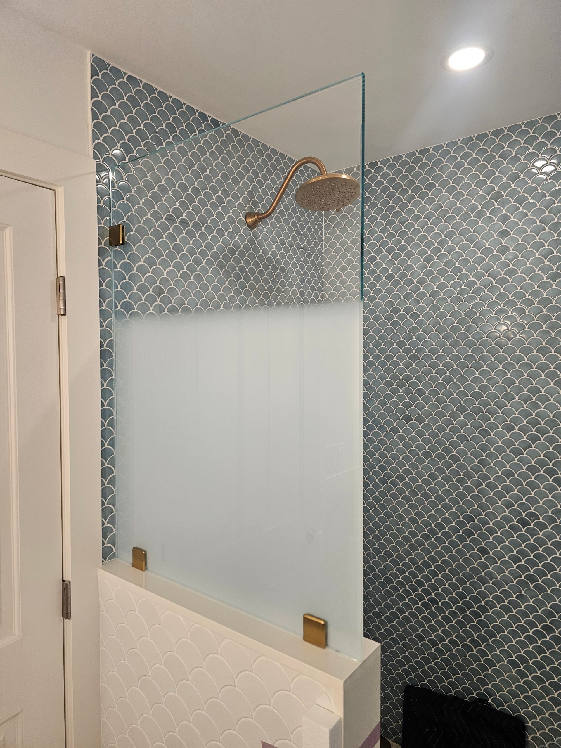 Glass shower with a frosted lower half and a gold showerhead, against blue-gray tiled walls.