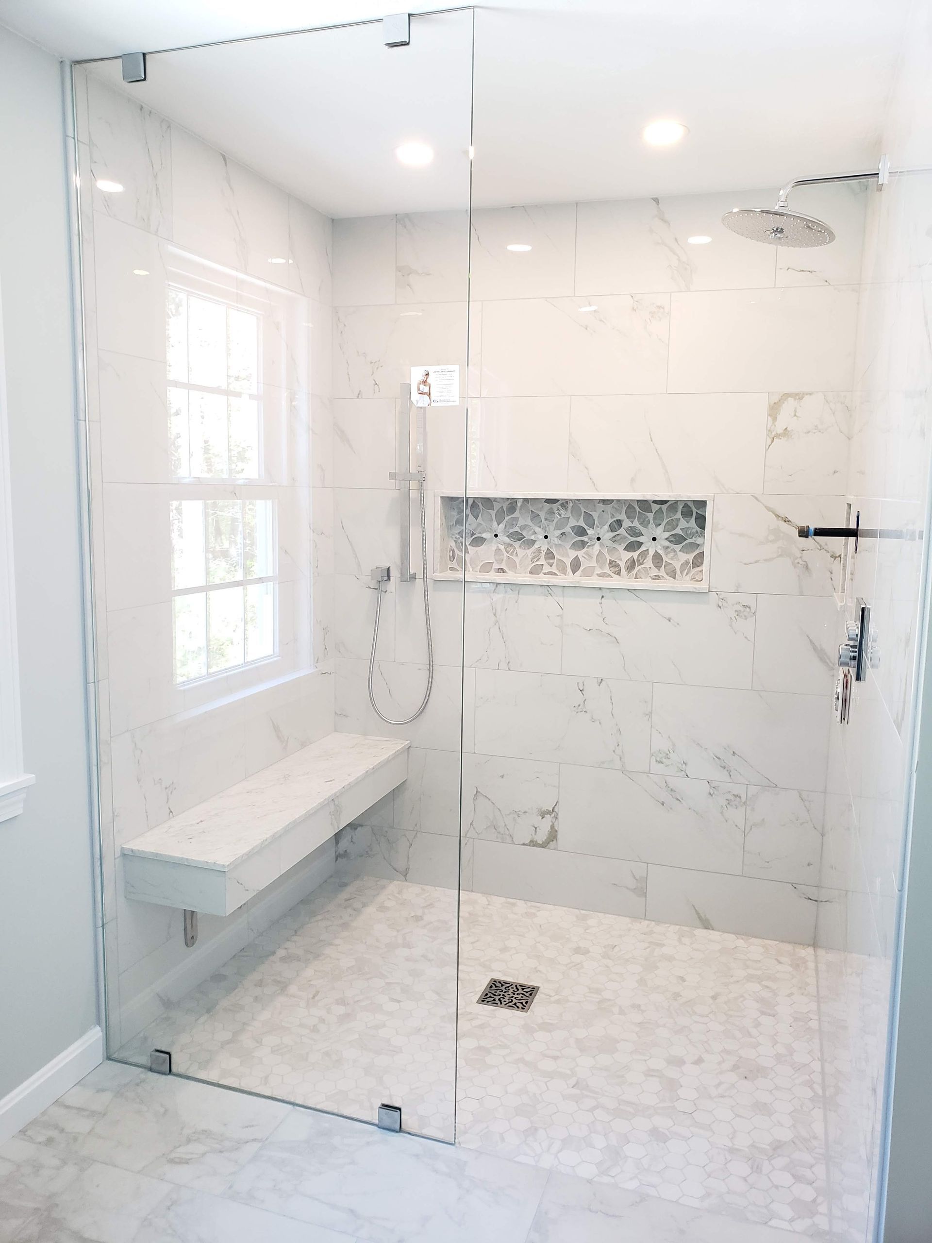 Modern, white-tiled shower with a glass door, built-in bench, and a small window.