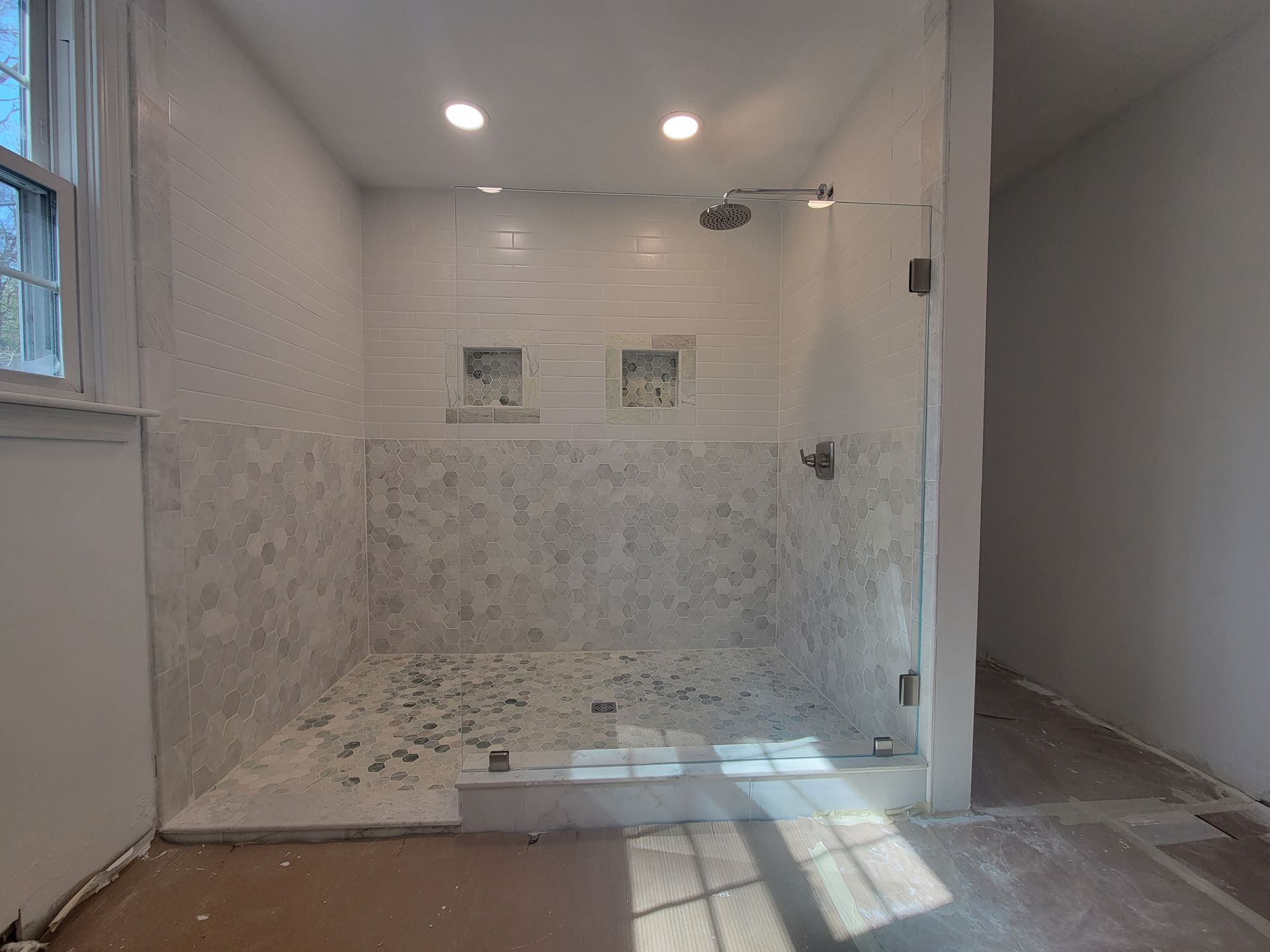 Newly renovated shower with glass door and stone tile interior.
