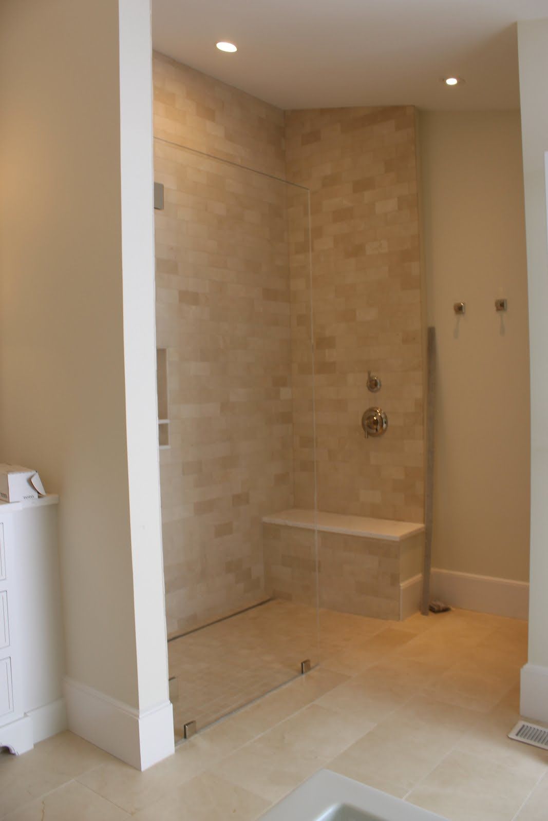 Modern bathroom with a tiled shower, glass door, and built-in bench. Cream walls and floor.