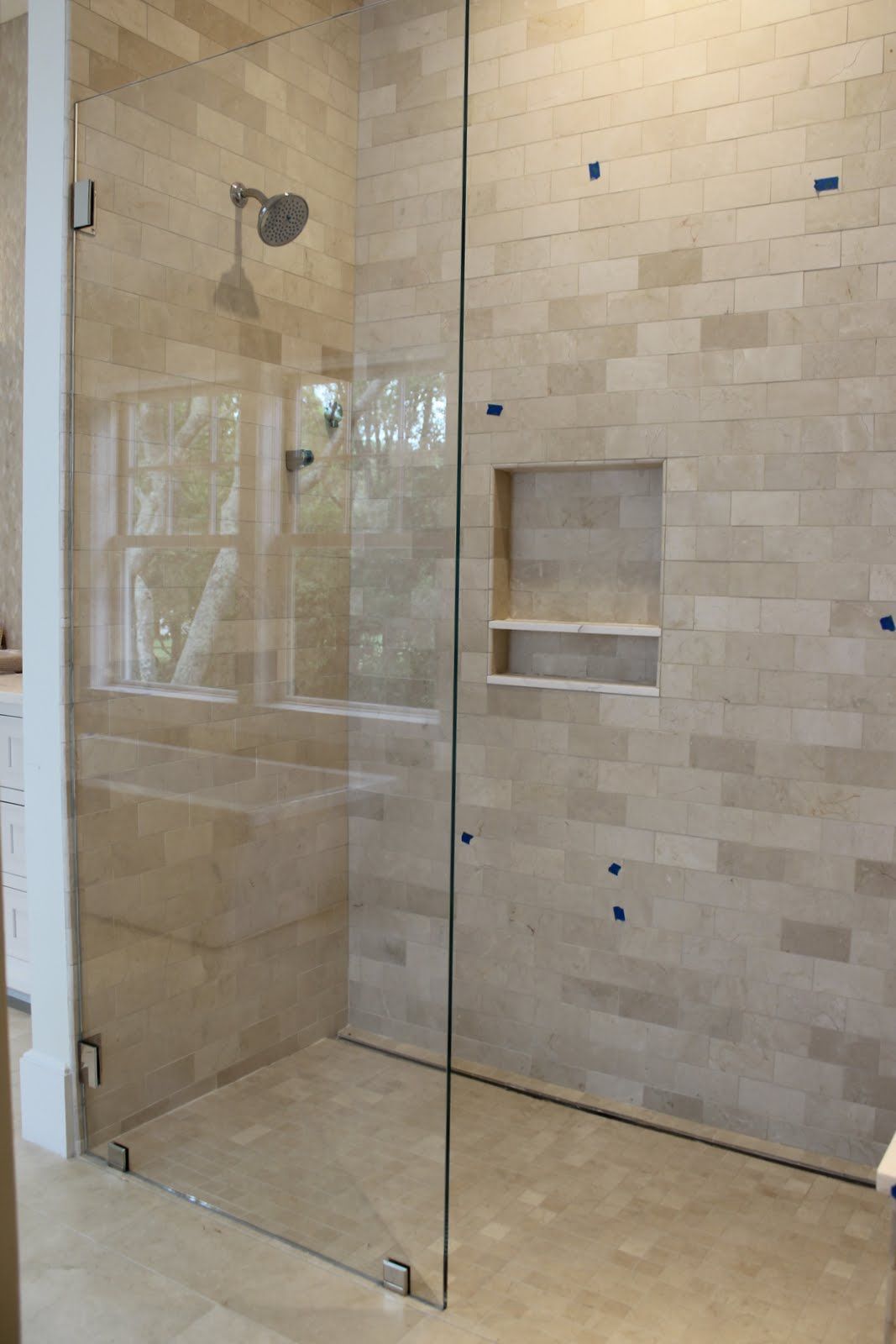 Glass shower enclosure with beige tile walls and recessed shelf.