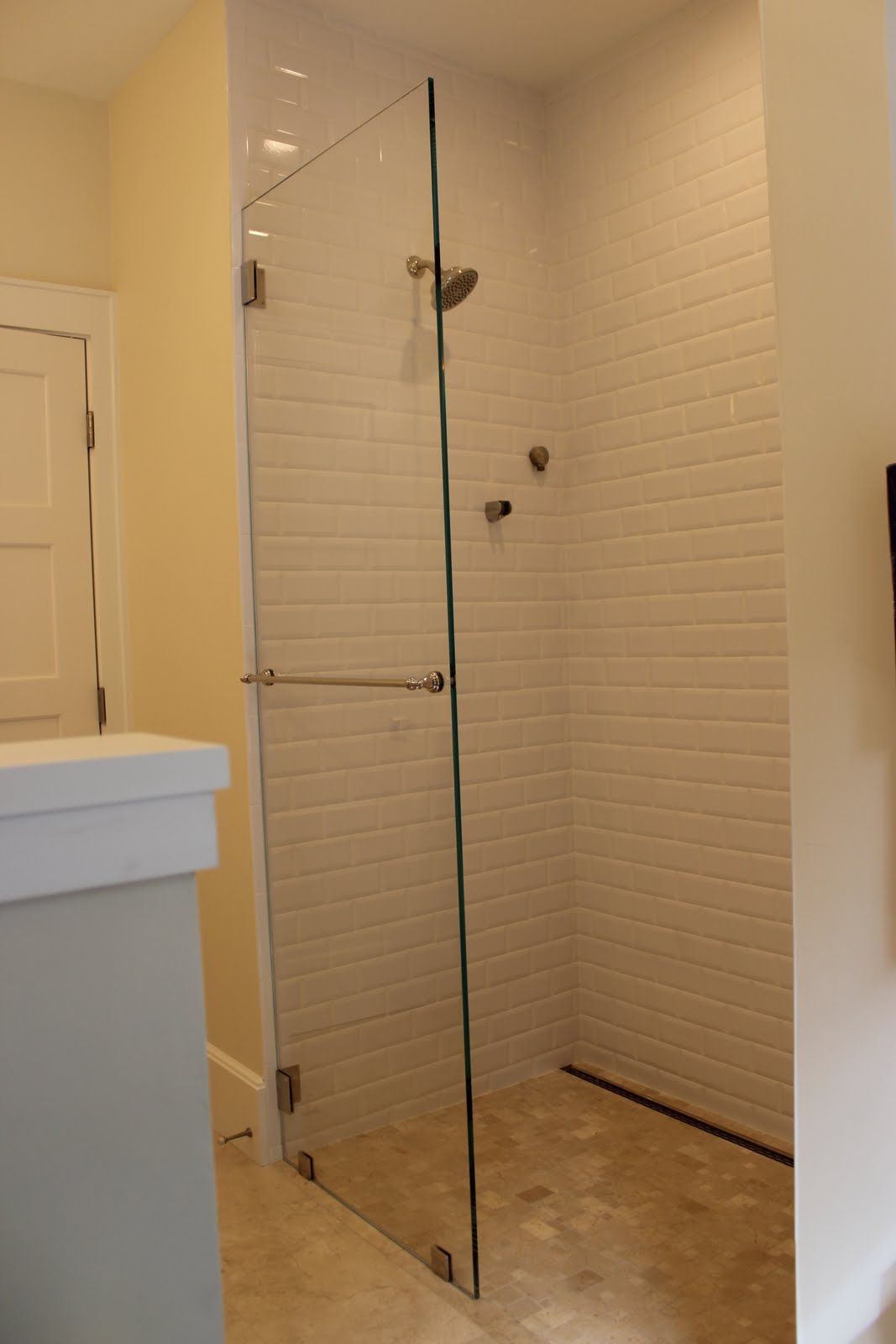 Glass shower enclosure with white brick-like tiles, a chrome shower head and bar handle.