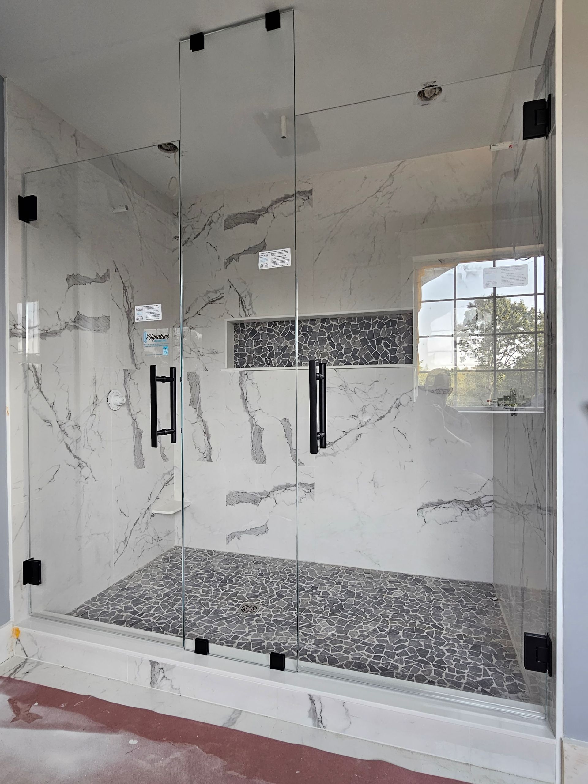 Glass shower enclosure with black hardware and marble tile interior.