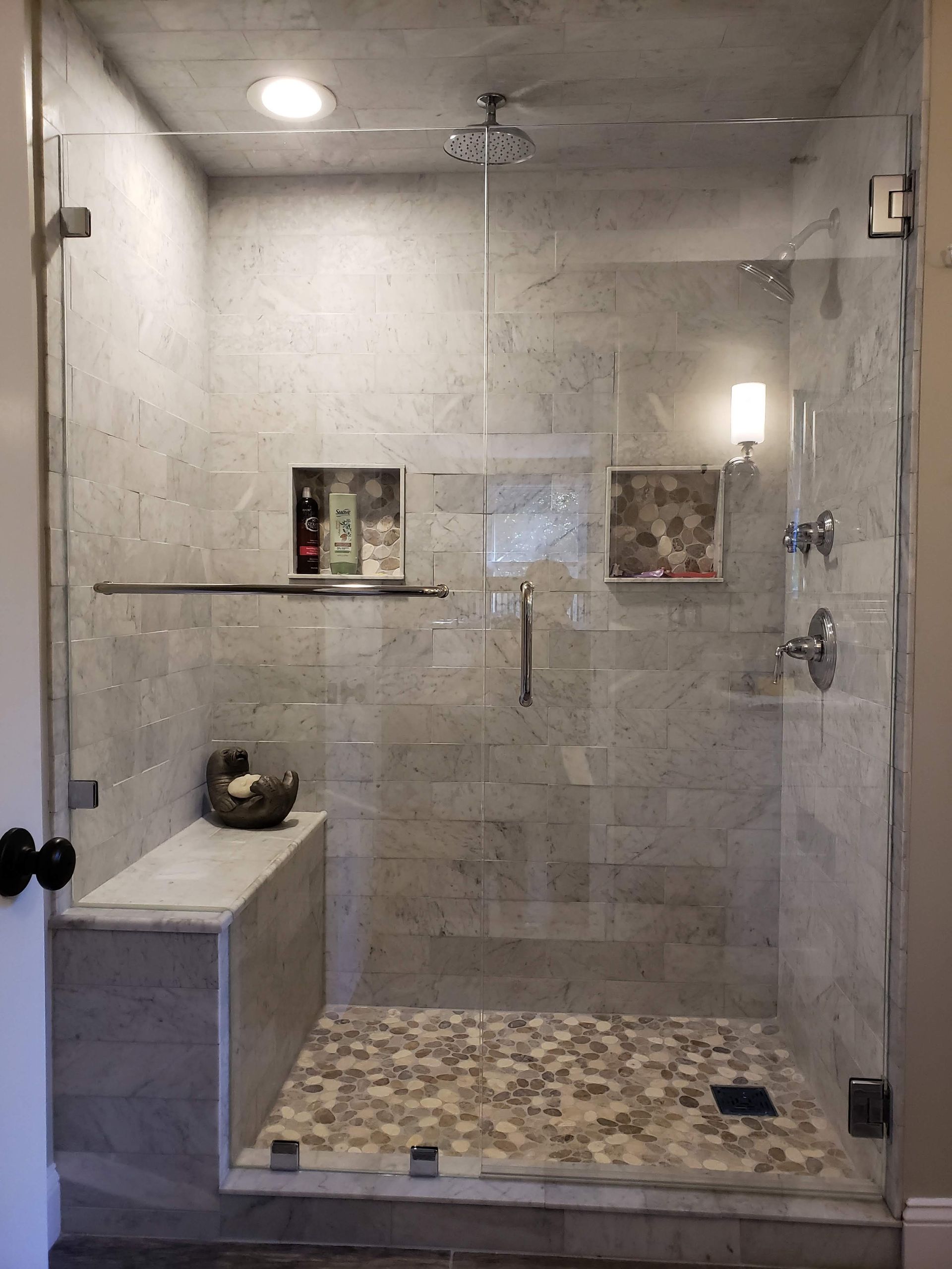 Modern shower with glass doors, stone tile walls and floor, built-in bench.