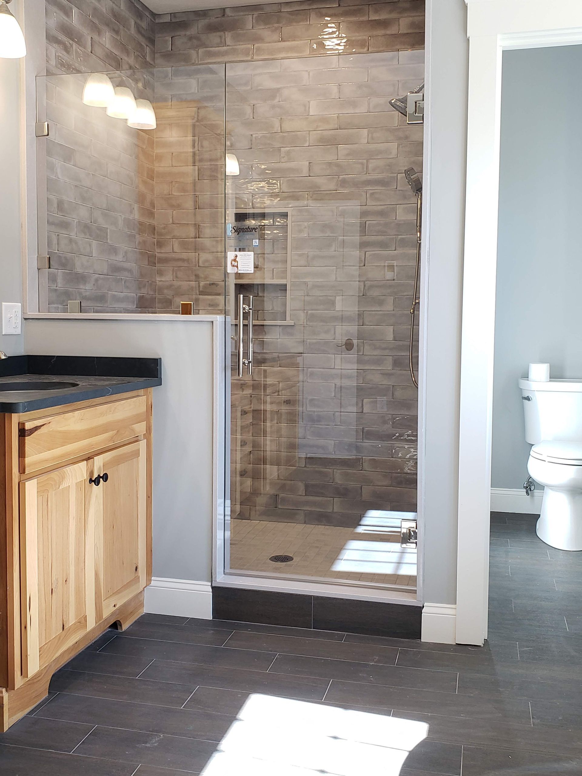 Bathroom with a glass shower, stone tile walls, wooden vanity, and a toilet.